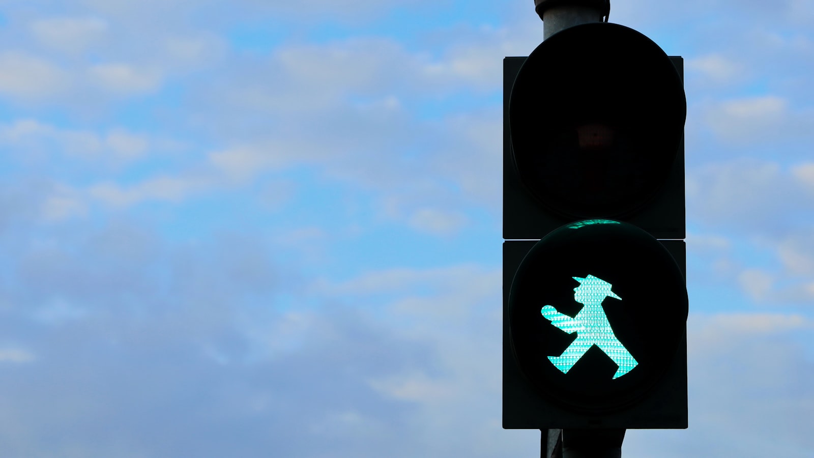 Grön gångsignal i en trafiksignal mot blå himmel