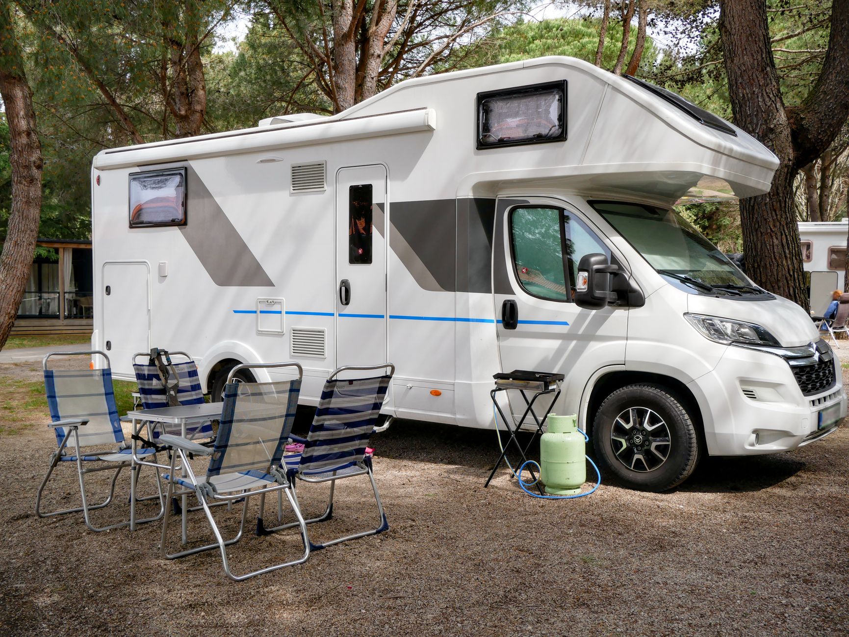 Vit alkovhusbil på en camping med campingstolar och grill framför