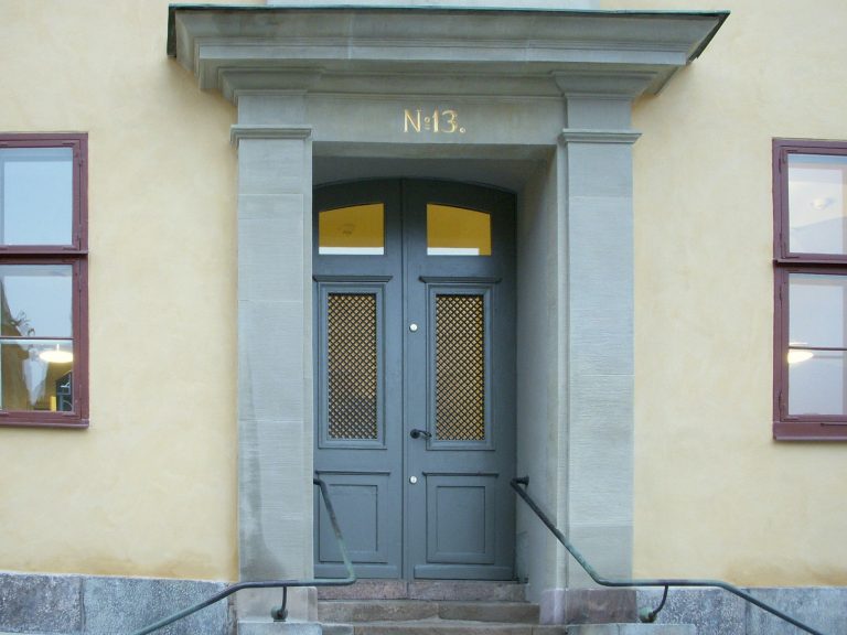 Gul putsfasad med grå stenportal och dubbeldörr, guldsiffran N:o 13 ovanför porten