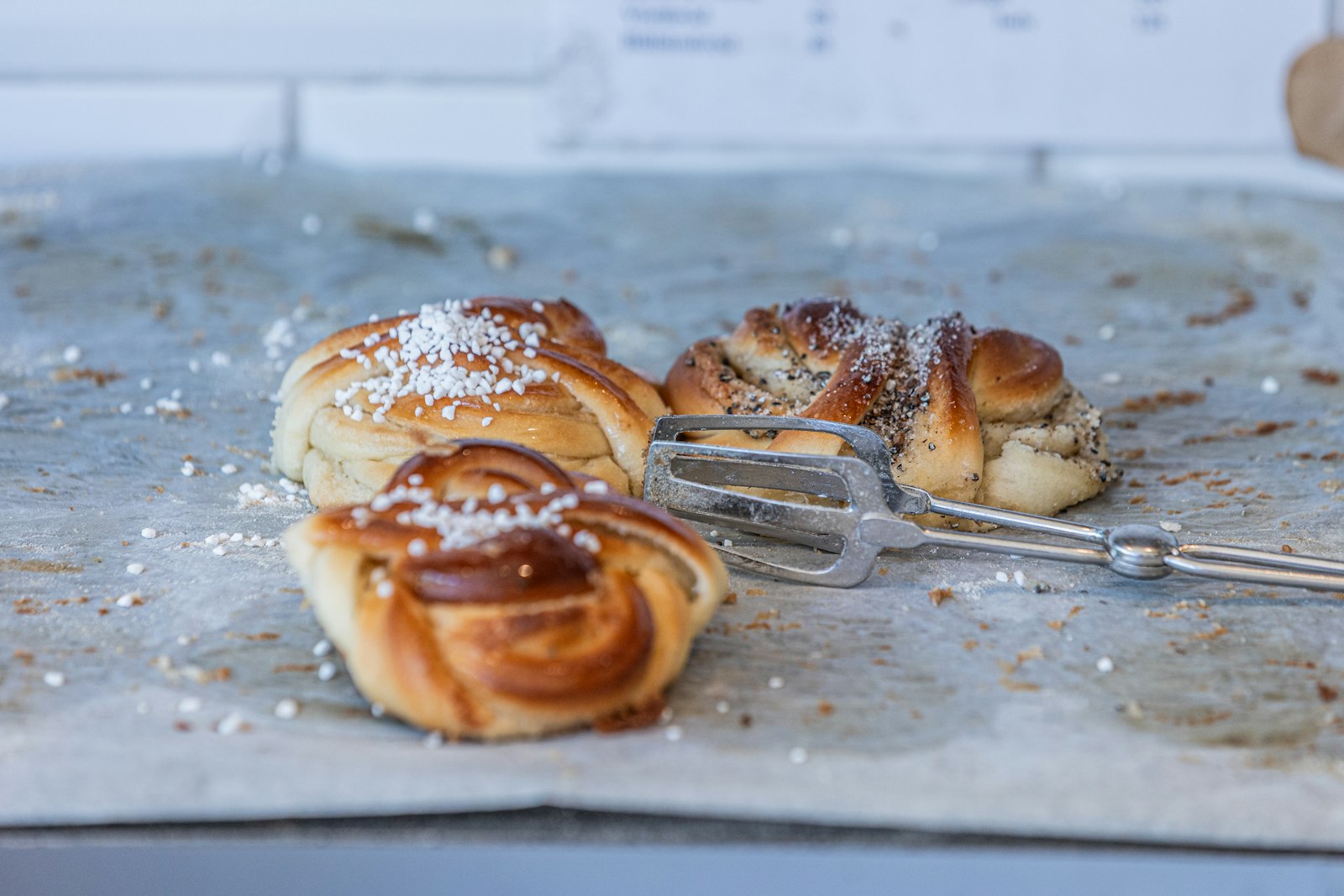 Nygräddade kanel- och kardemummabullar med pärlsocker på bakplåtspapper.