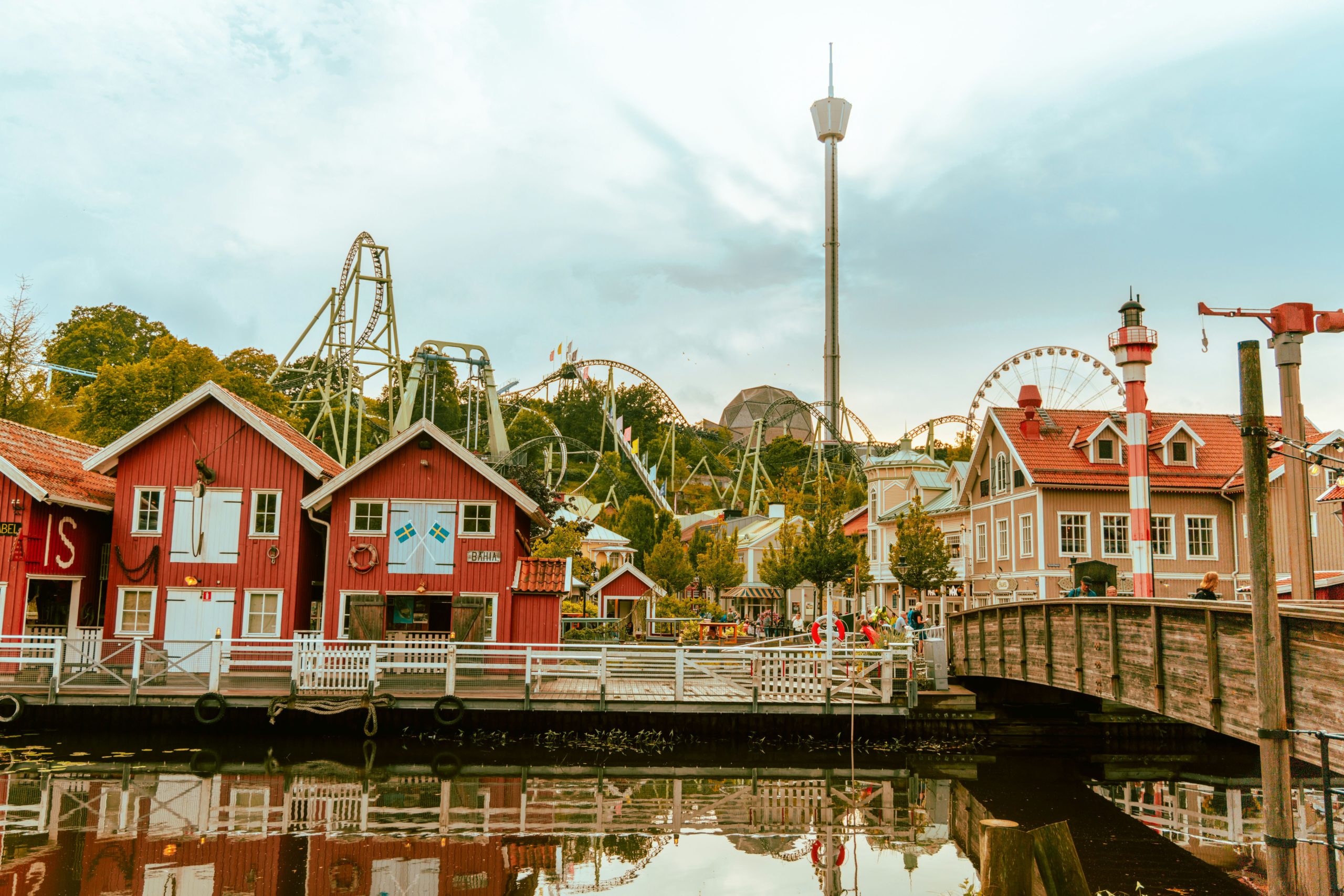 Röda trähus, berg- och dalbana och Lisebergstornet speglade i vattnet på Liseberg i Göteborg