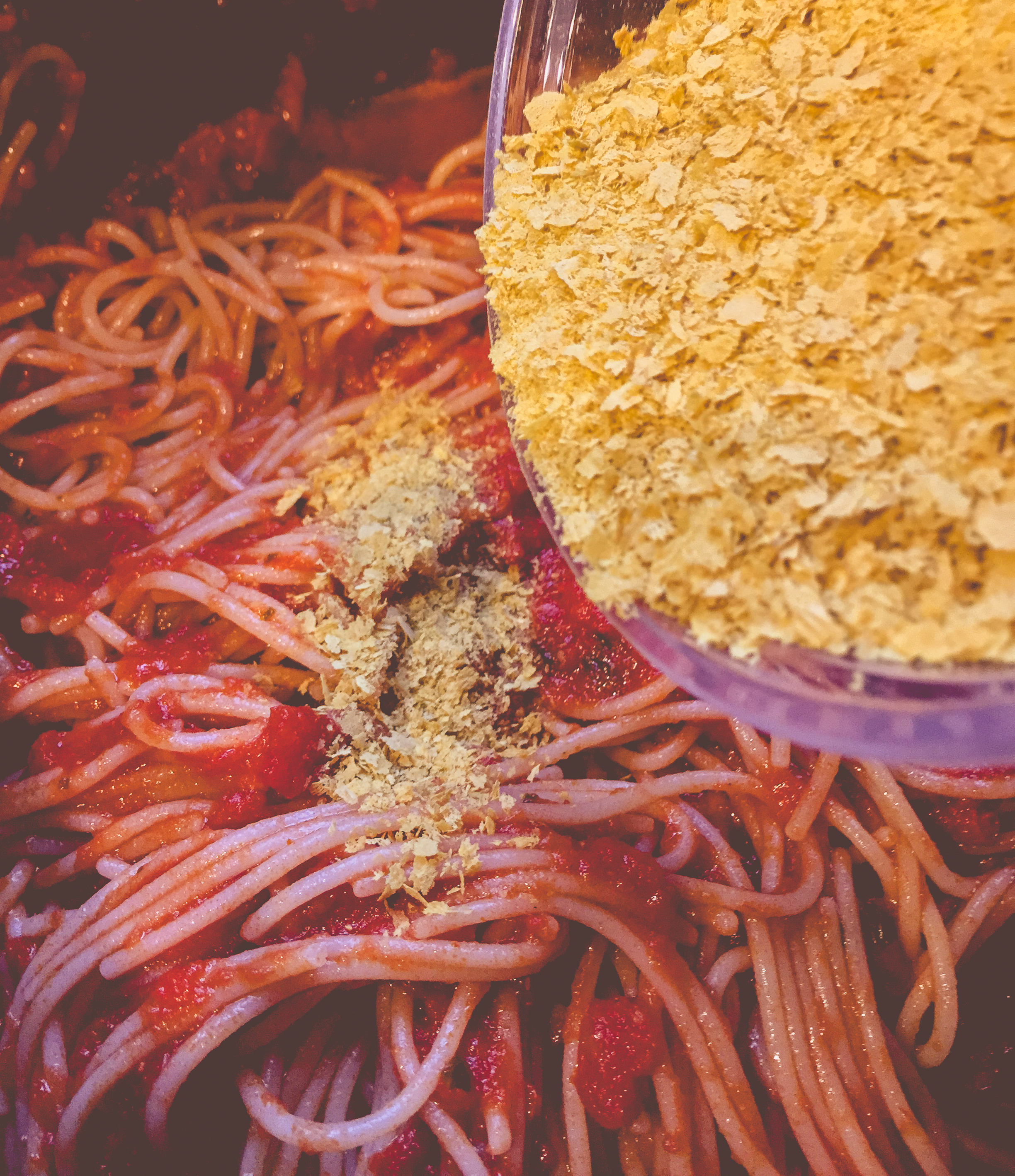 Gula flingor av näringsjäst strös och hälls över spaghetti med tomatsås, som ett veganskt parmesanalternativ