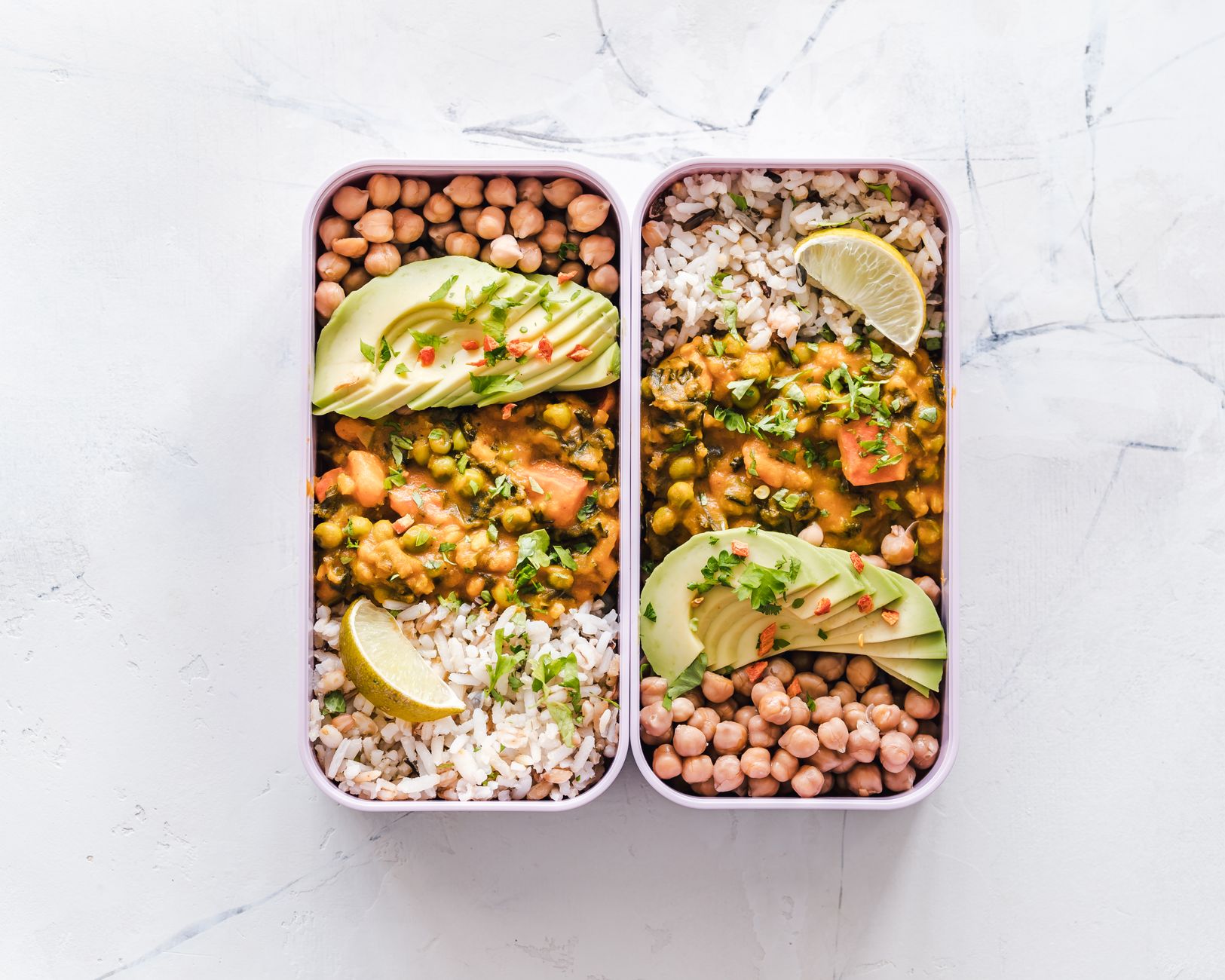 Färgglada vegankomponerade lunchlådor med kikärter, curry med ärtor, avokado, ris och lime