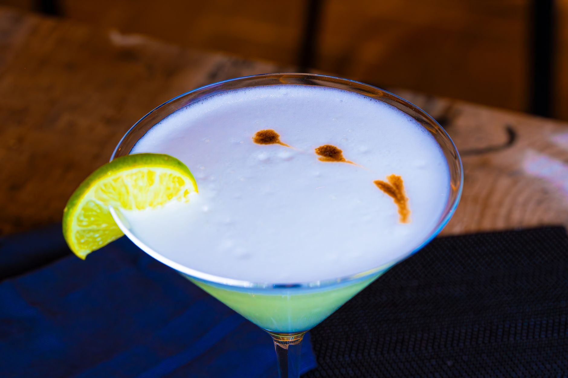 Pisco sour med vit skumkrona och bitterdroppar ovanpå, limeklyfta som garnering