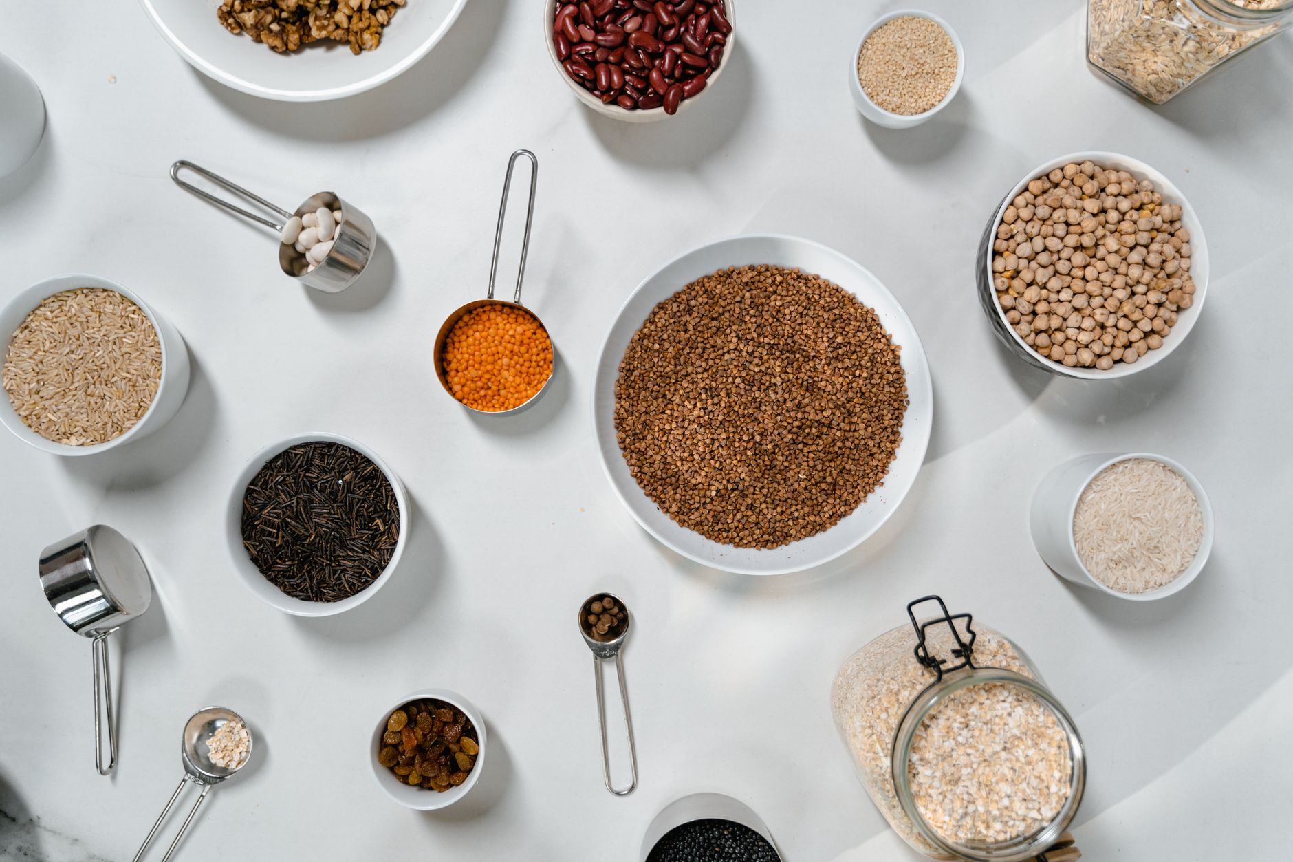 Veganskt skafferi med baljväxter, spannmål och nötter i skålar: valnötter, kidneybönor, kikärter, ris, linser och bovete
