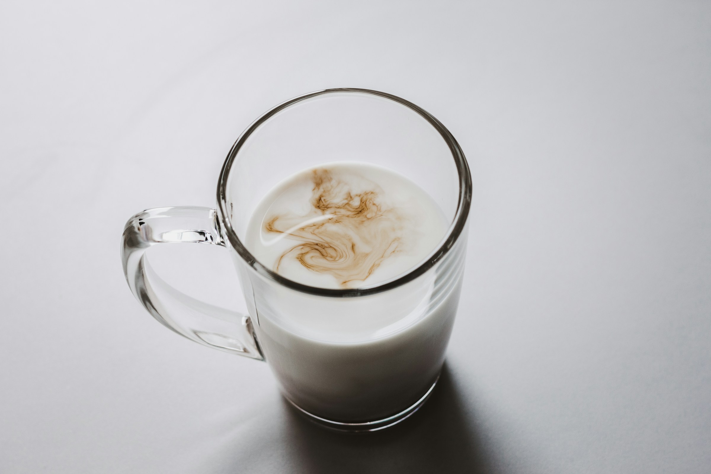Ett glas med ljus dryck där kaffe virvlar in, på en grå bordsyta