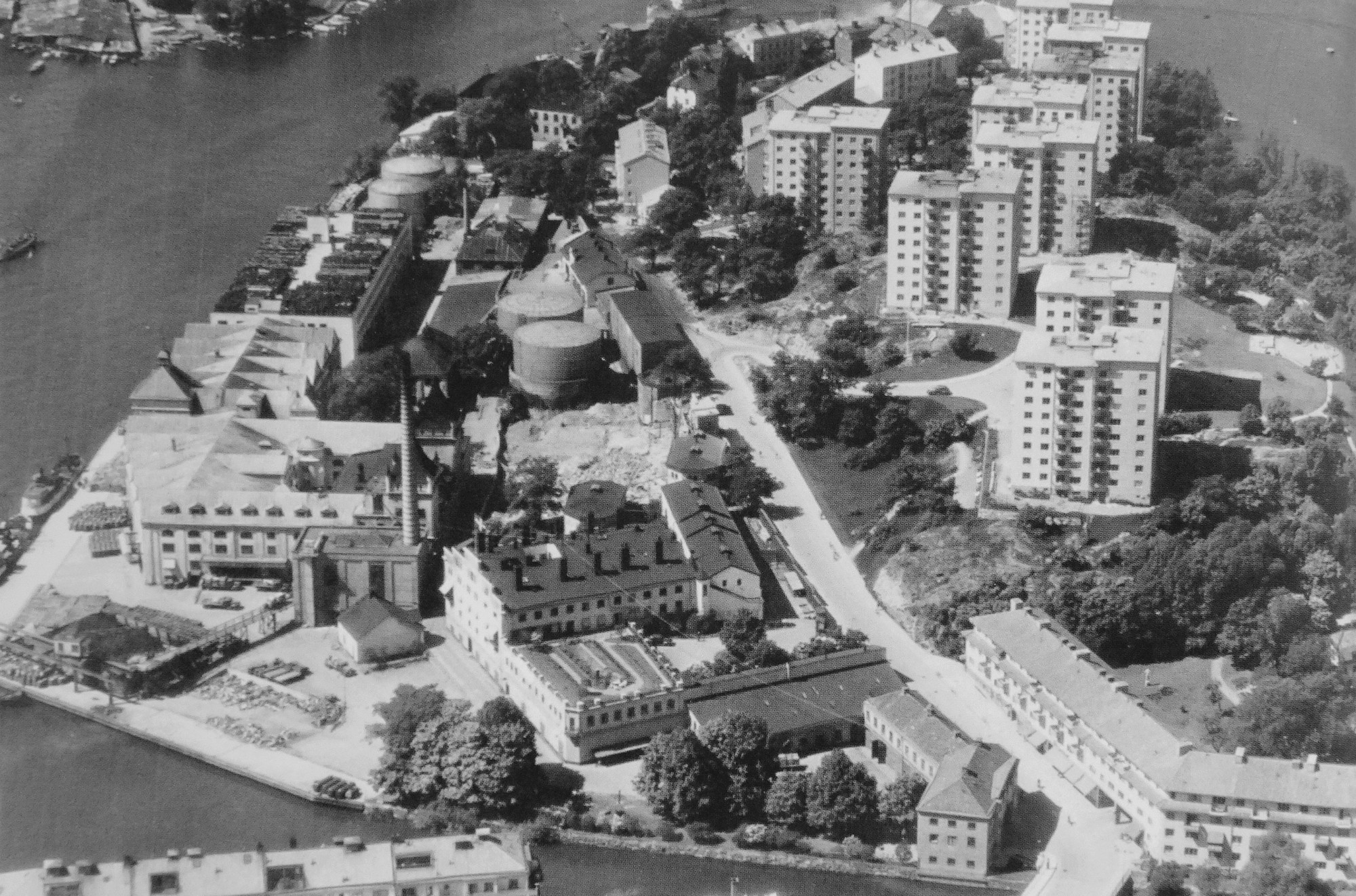 Flygfoto över Reimersholme 1945 med spritfabrikens byggnader och cisterner till vänster och HSB:s punkthus på berget till höger.