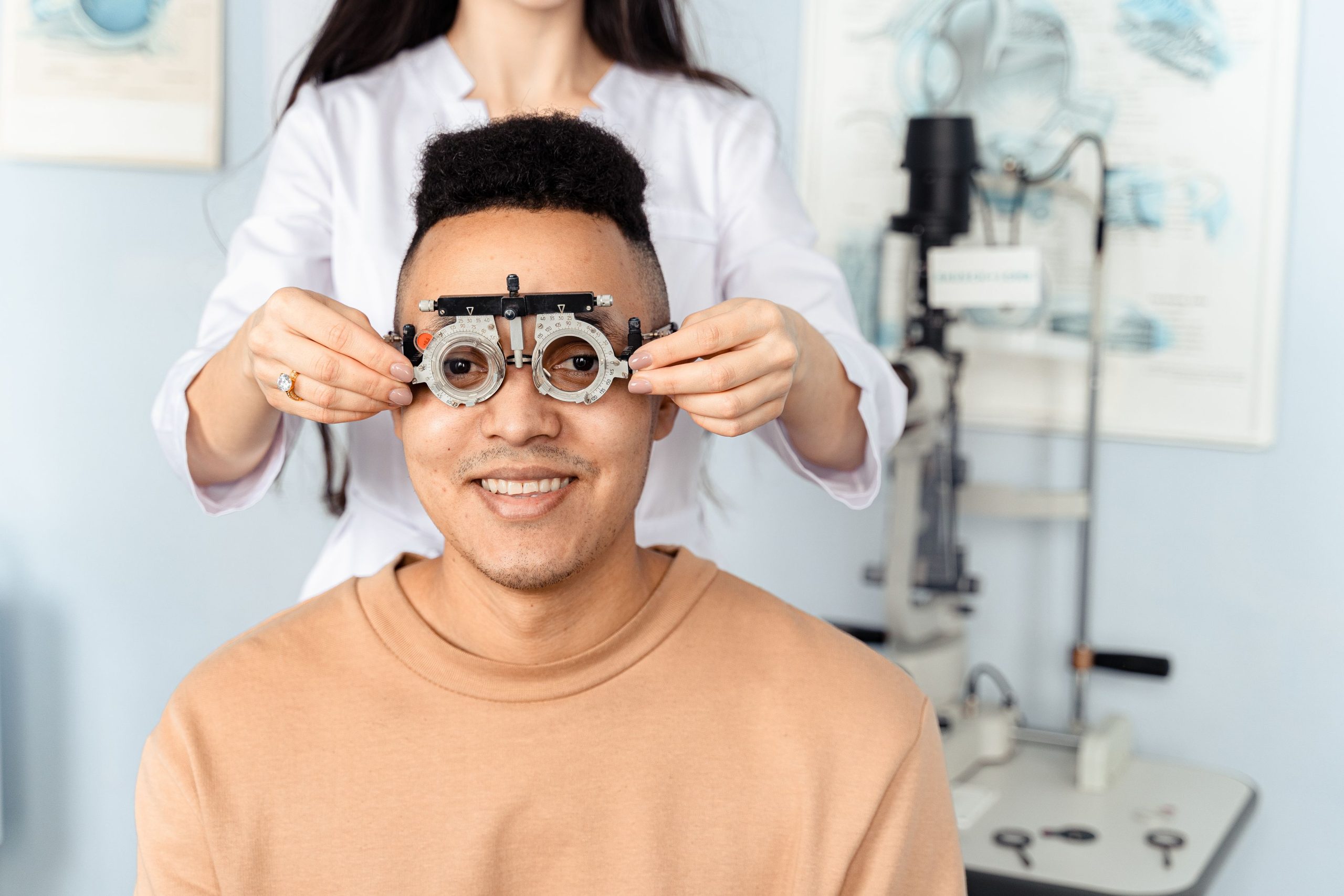 An optician holds a trial frame in front of a smiling man during an eye examination