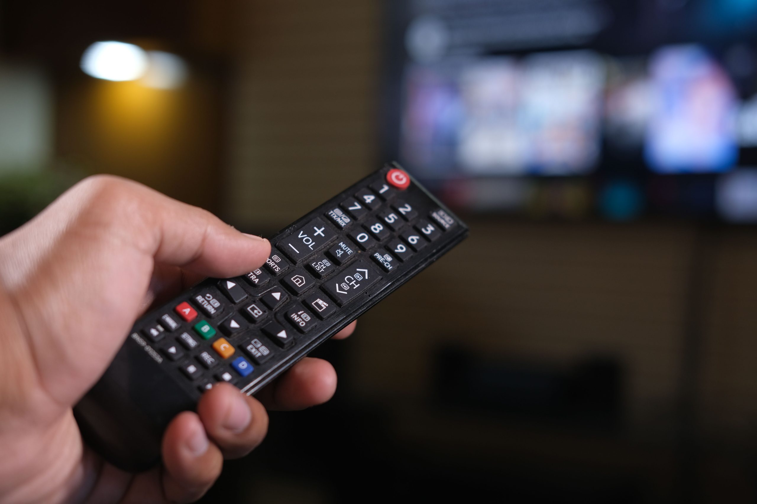 Hand med fjarrkontroll framfor en tv med streamingtjanst