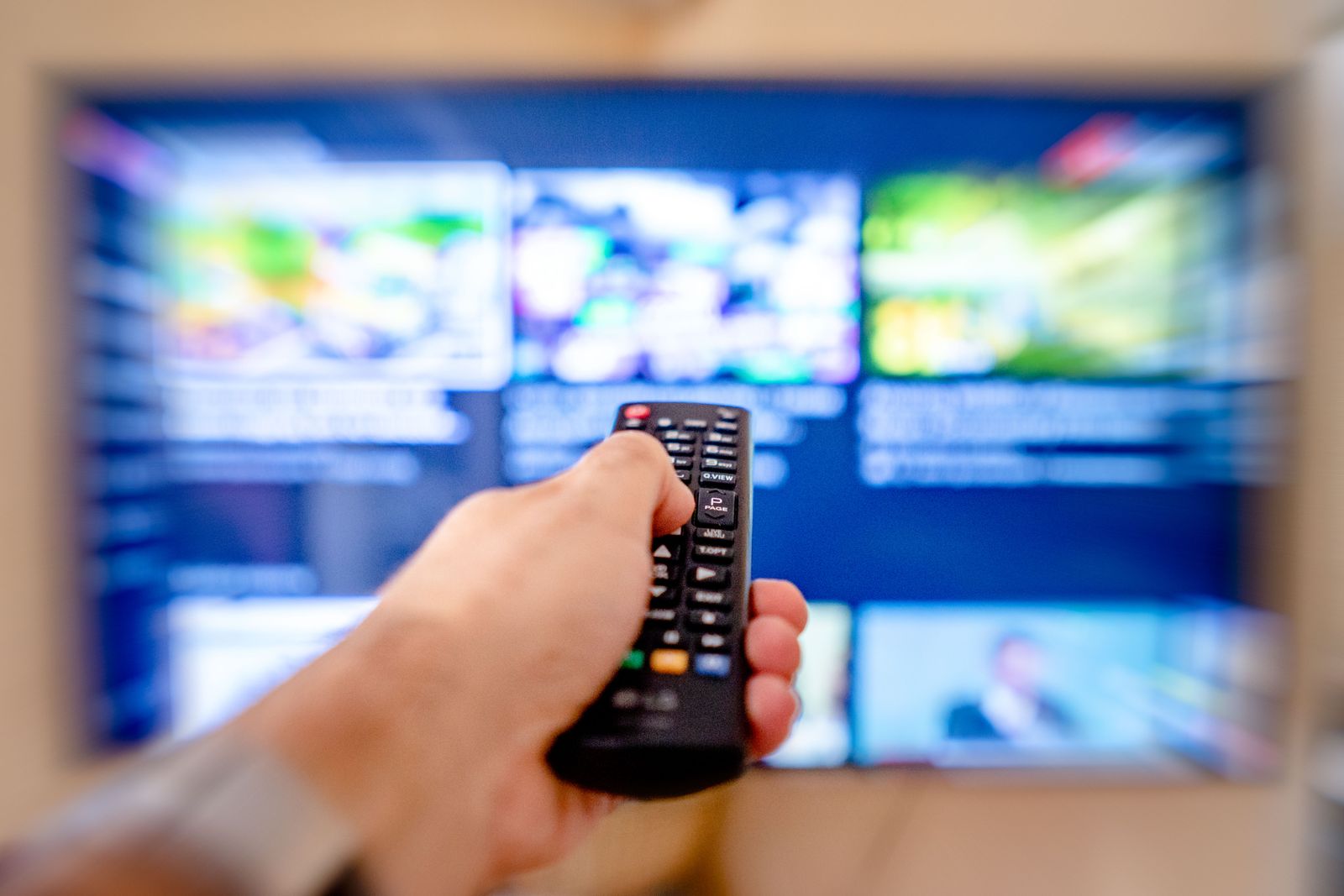 Hand som håller en tv-fjärrkontroll riktad mot en tv-skärm