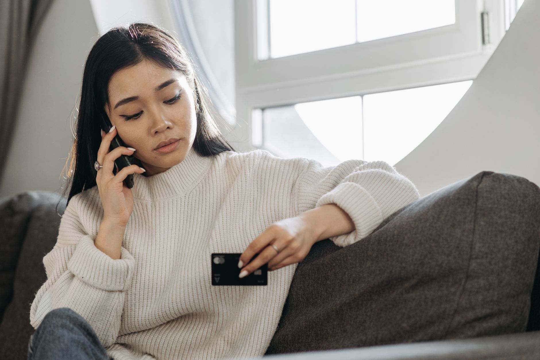 Kvinna i soffa med telefonen mot örat och ett betalkort i handen