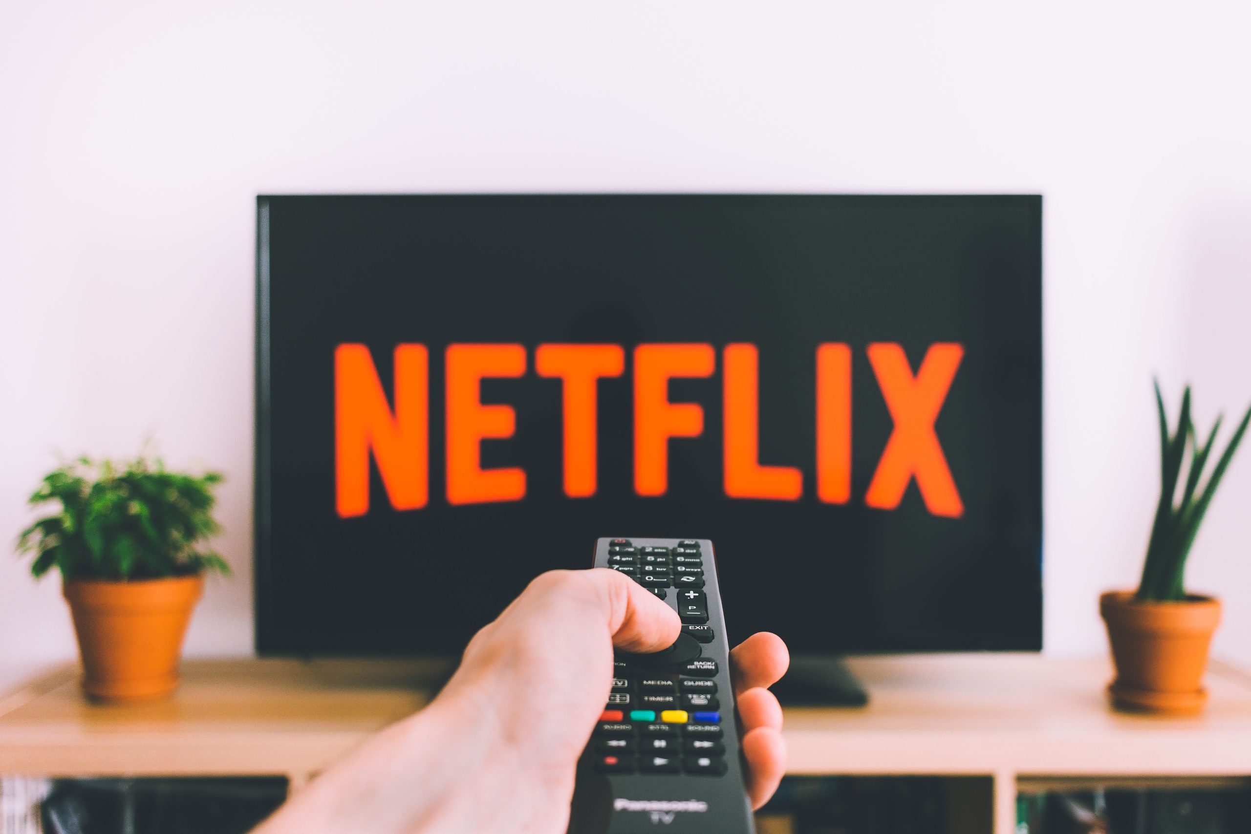 Hand som riktar en fjärrkontroll mot en tv där Netflix startskärm visas