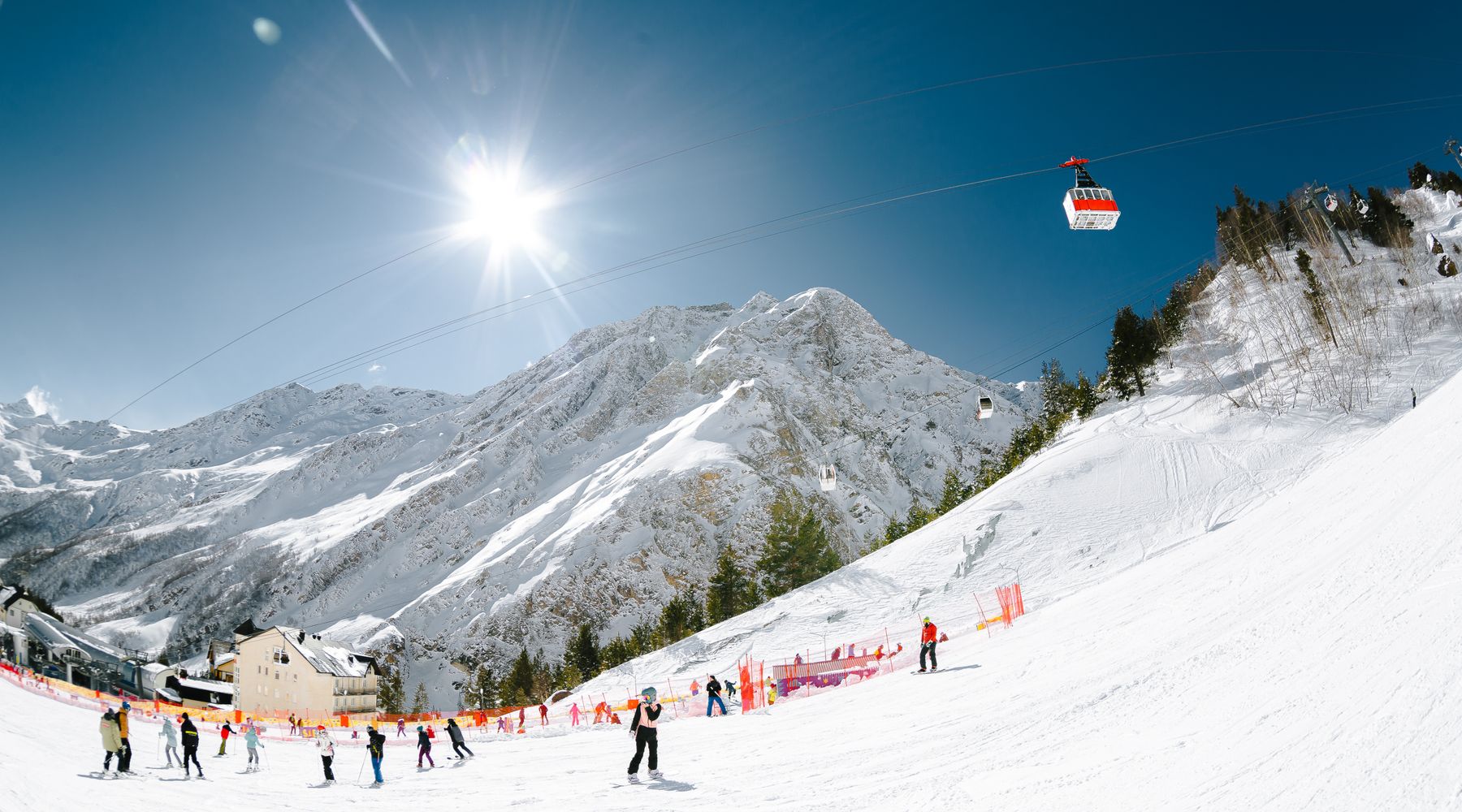 Solig pist i en alpin skidort med skidåkare och gondol