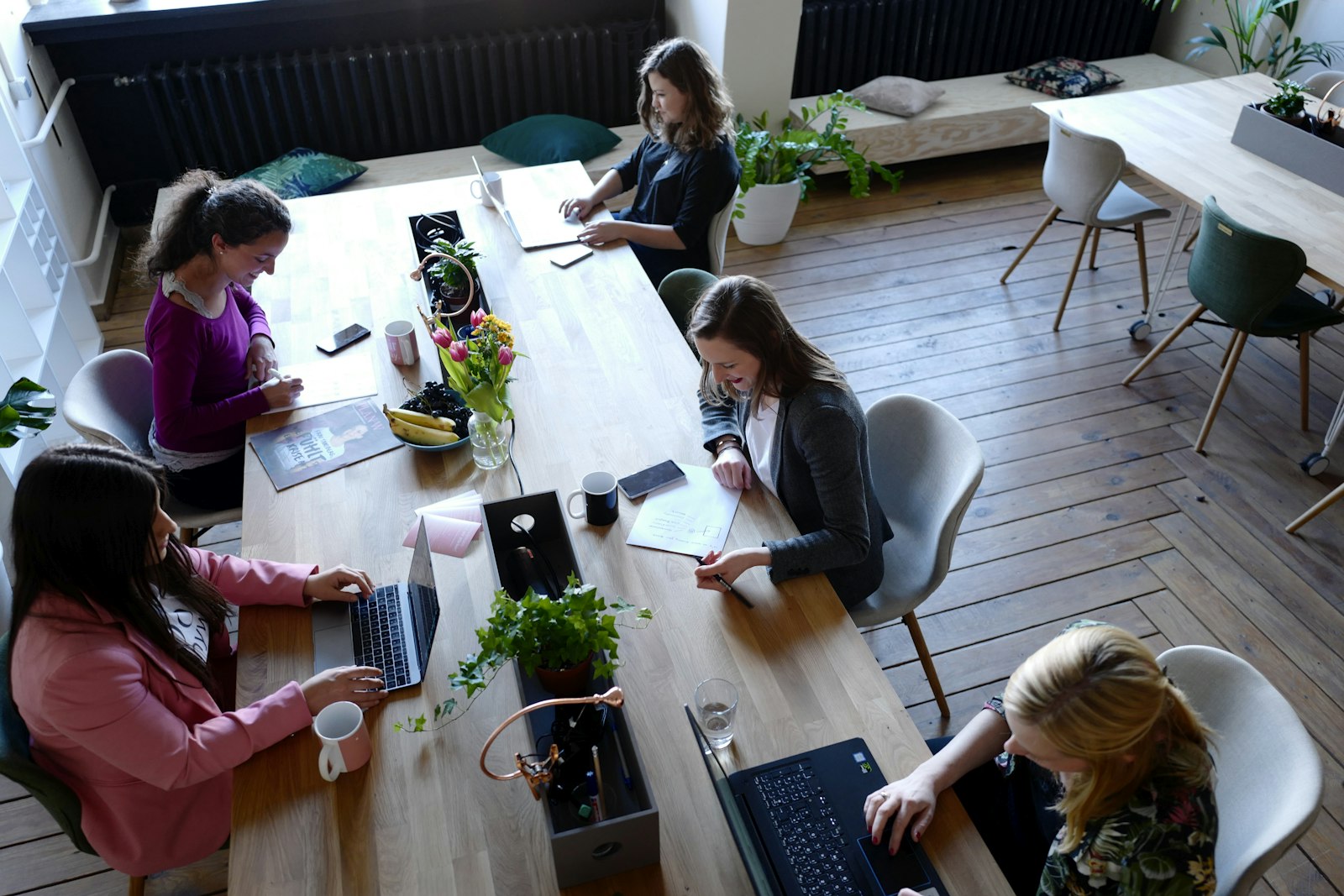 Fem personer arbetar vid ett långt delat träbord i ett coworkingkontor