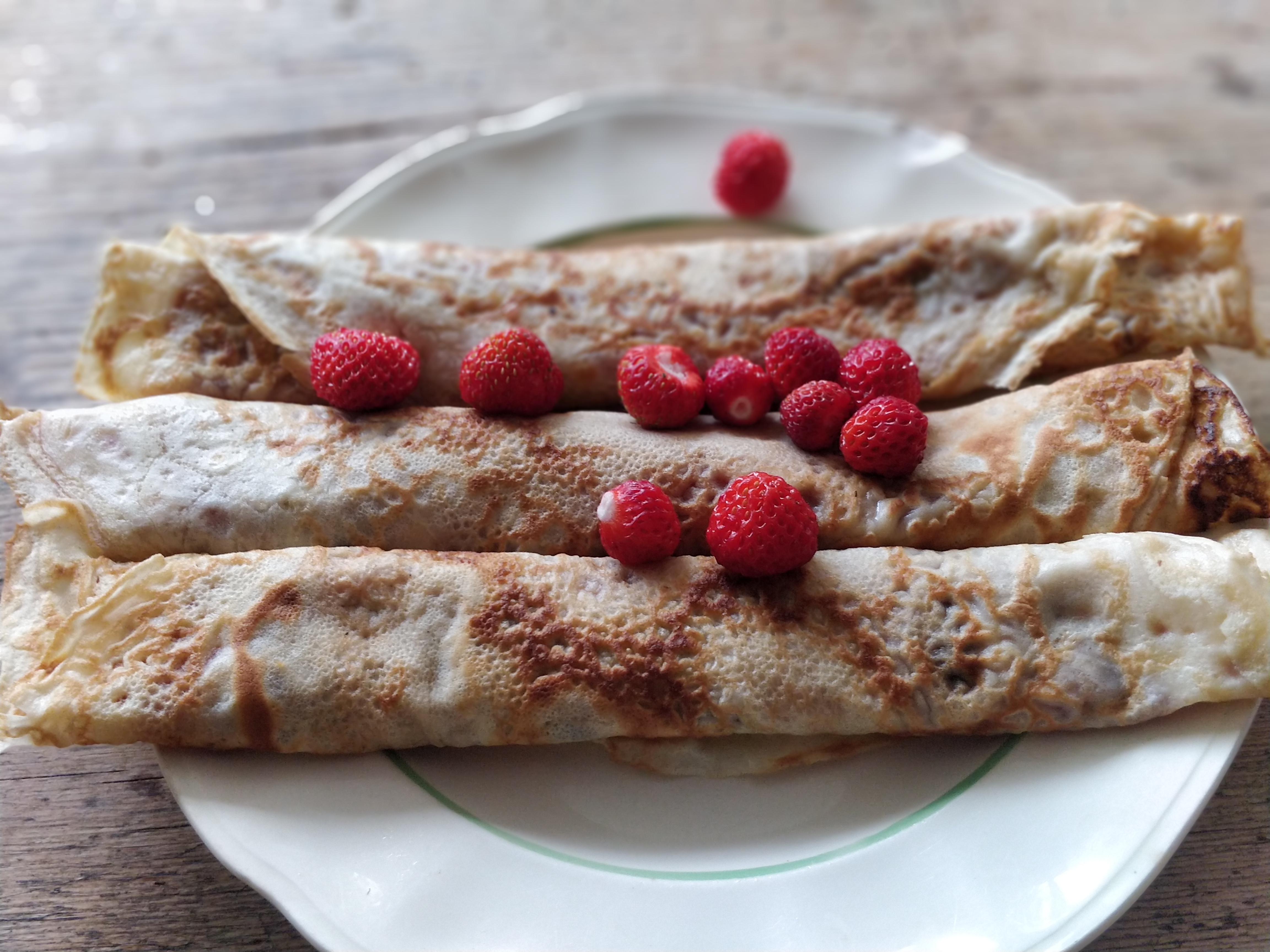 Thin rolled Swedish pancakes with wild strawberries on a plate