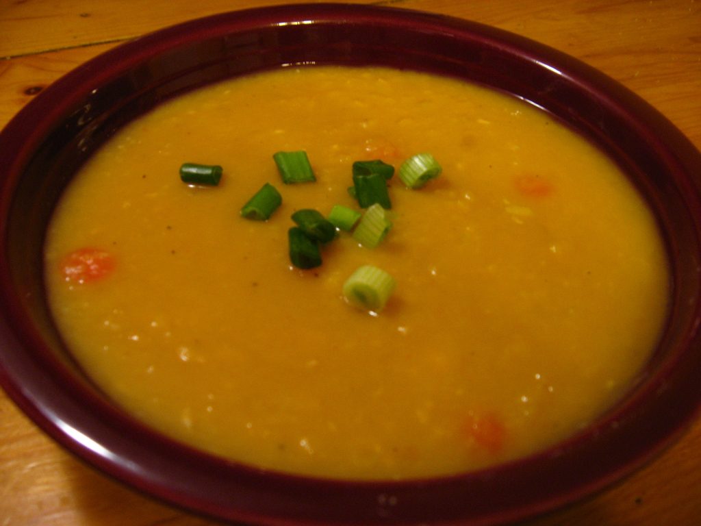A bowl of thick yellow split pea soup topped with spring onion