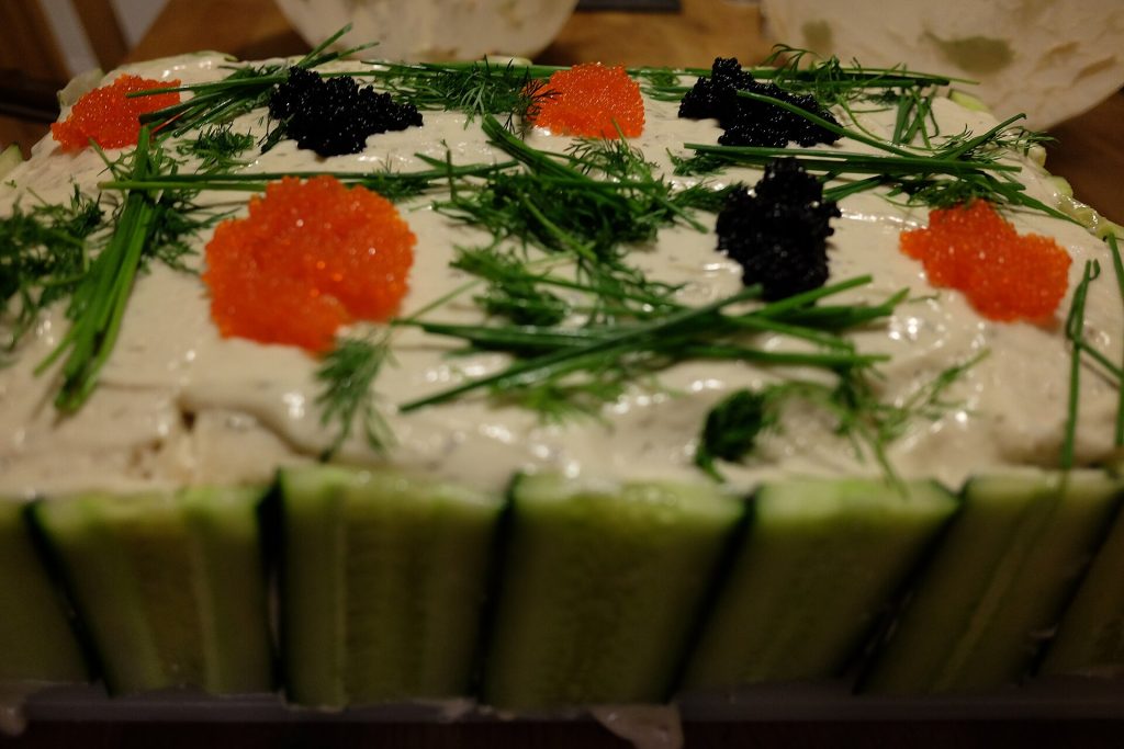 Vegan smörgåstårta with cucumber-lined sides, topped with red and black seaweed caviar, dill and chives