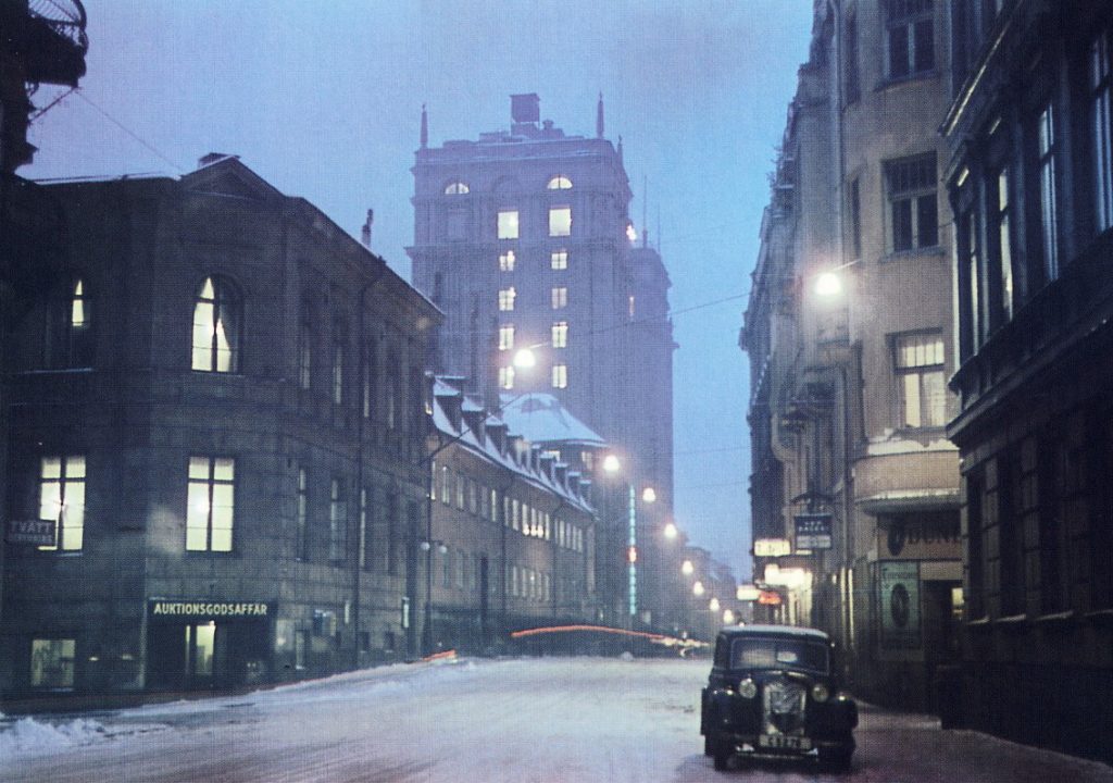 Malmskillnadsgatan i vinterskymning 1946, snötäckt gata med upplysta fönster och en bil