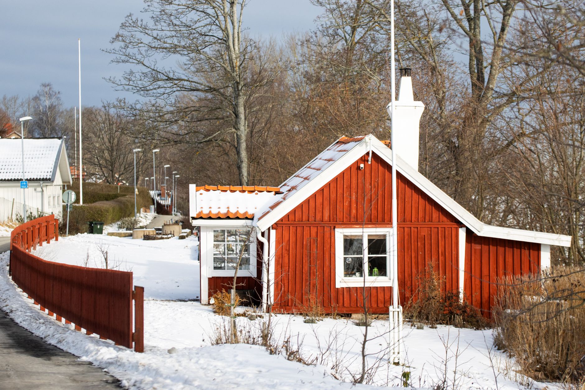 Liten röd stuga med vita knutar i snö bakom ett rött staket