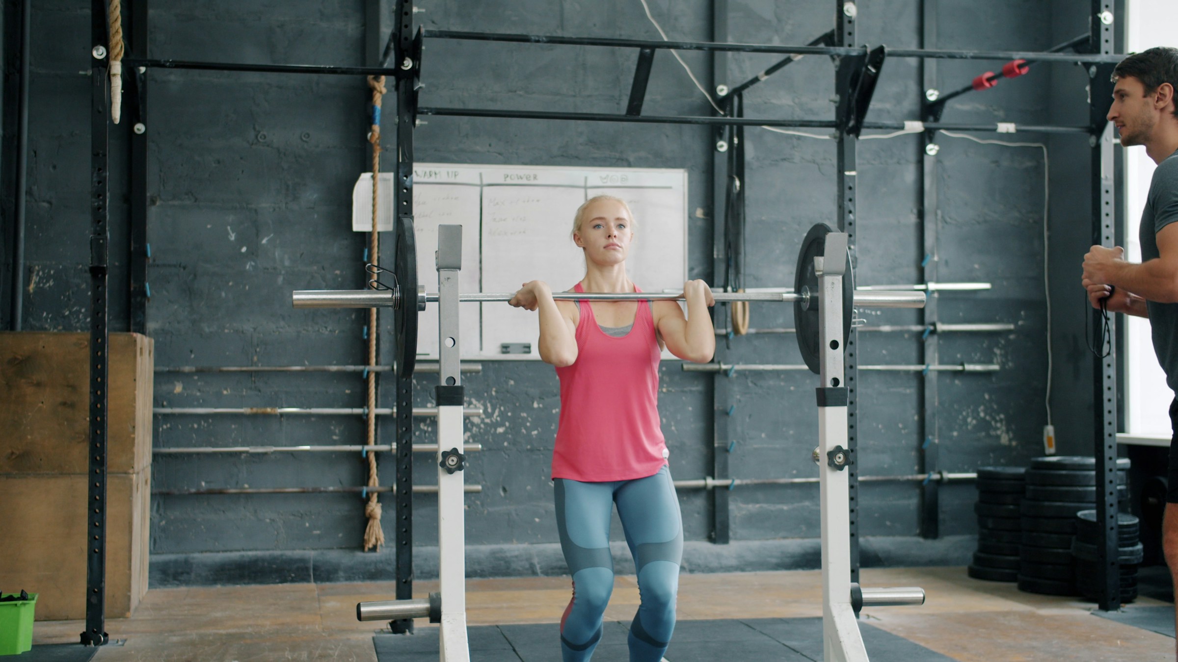 Kvinna lyfter skivstång i ett gym med en tränare i bakgrunden