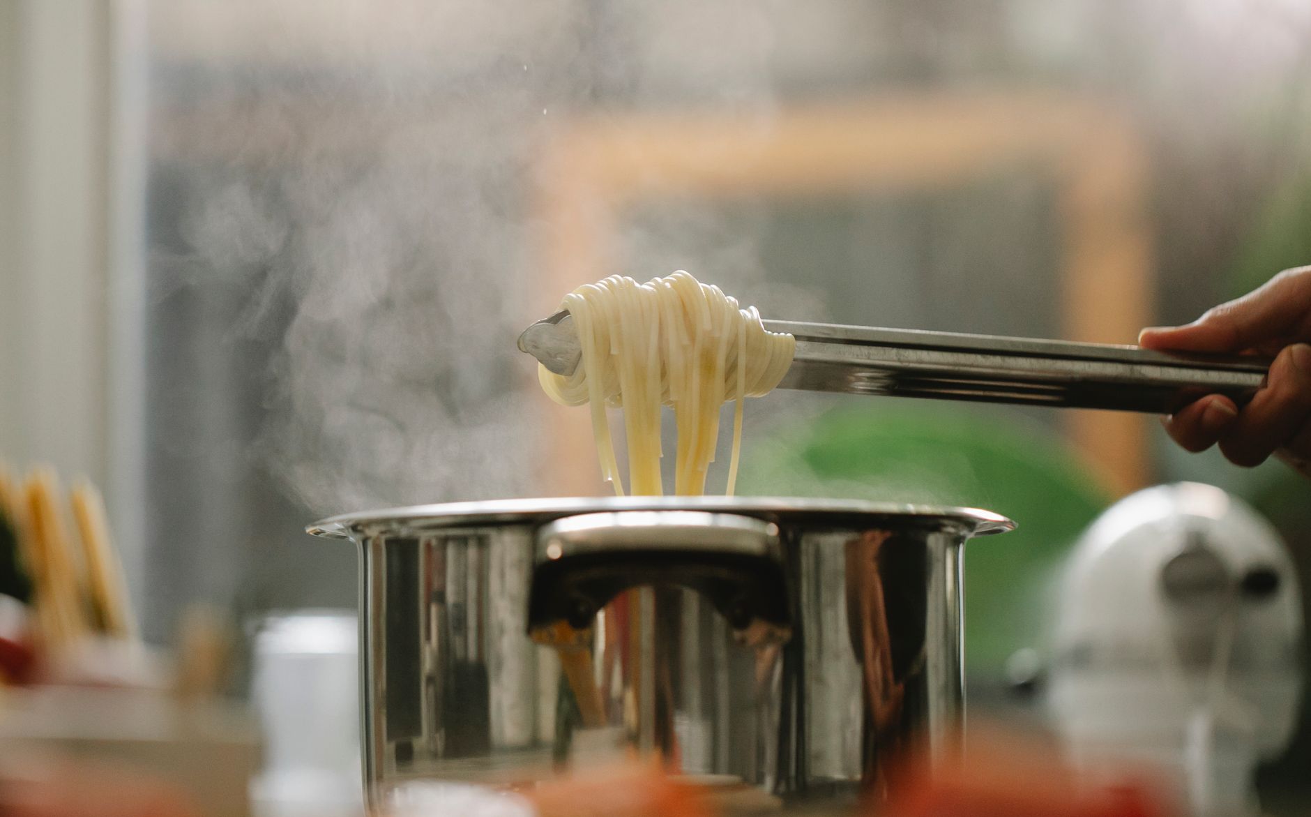Kokt spaghetti lyfts med tång ur en kastrull med kokande vatten