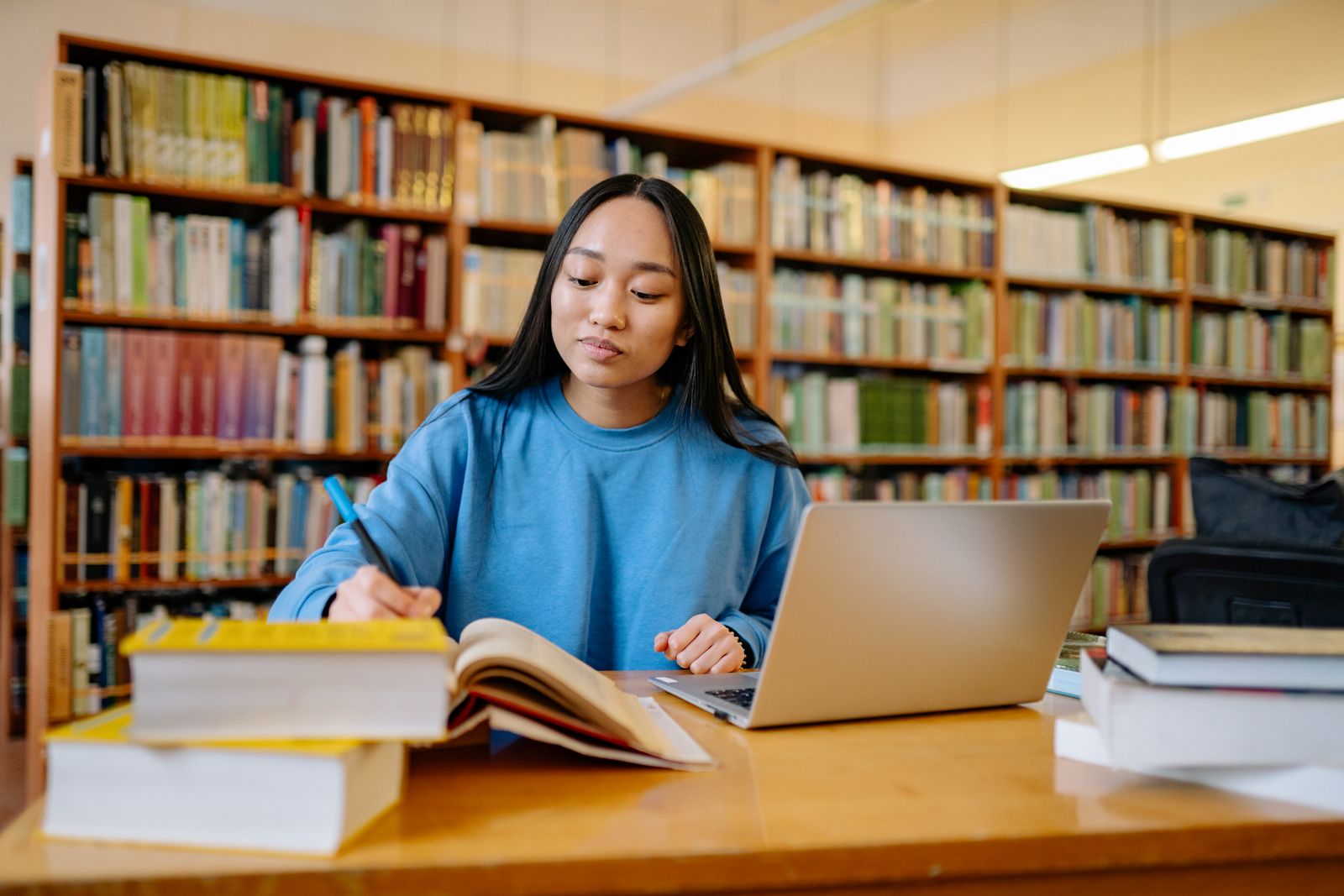 Ung kvinna studerar med böcker och dator i ett bibliotek