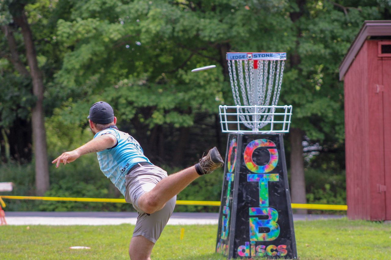Spelare kastar disc mot en discgolfkorg i en grön park
