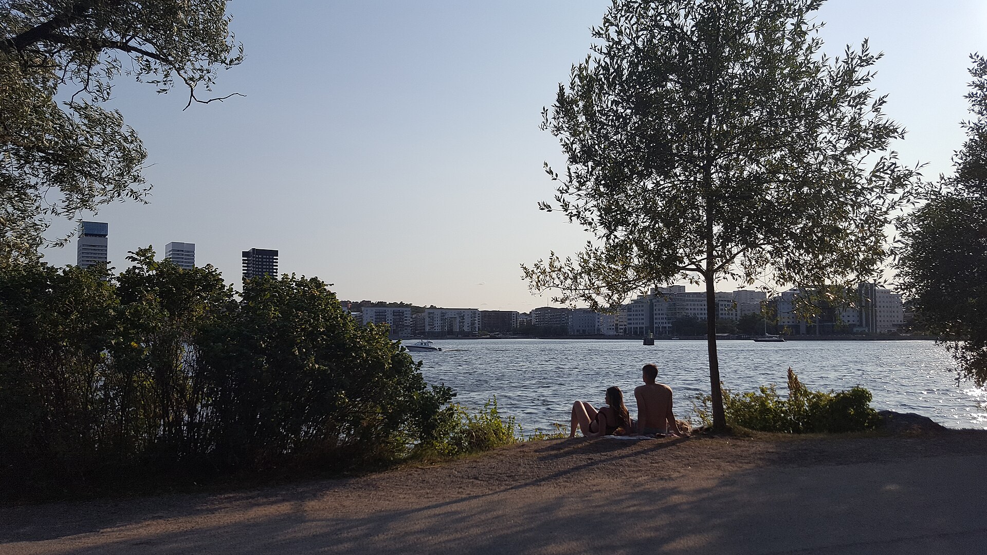 Människor sitter vid Årstaviken i Tantolunden en sommarkväll