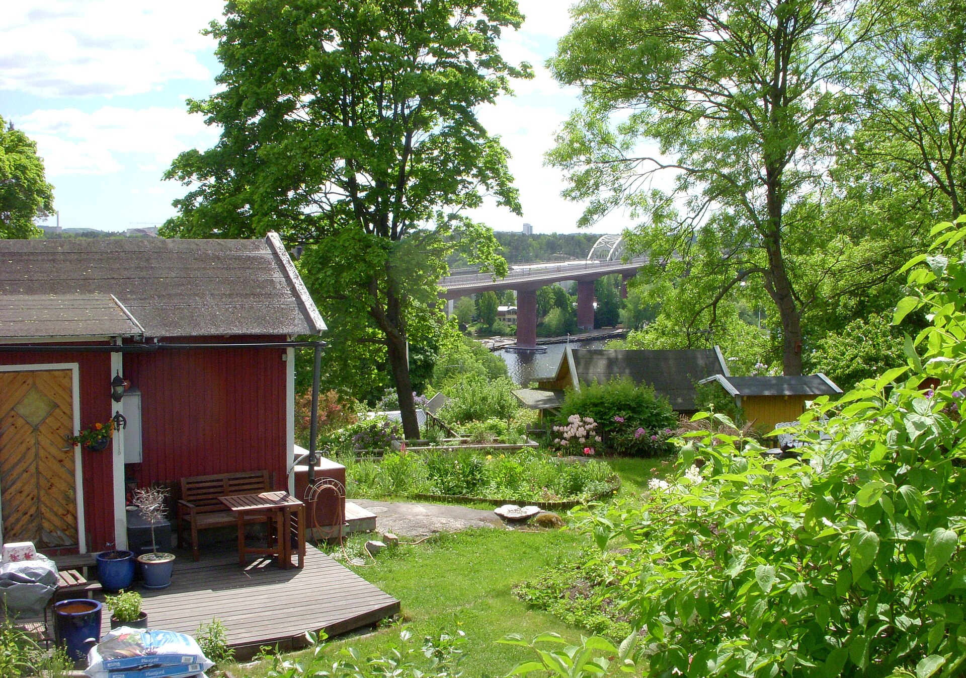 Röd kolonistuga med trädgård i Tantolunden, Årstabroarna i bakgrunden