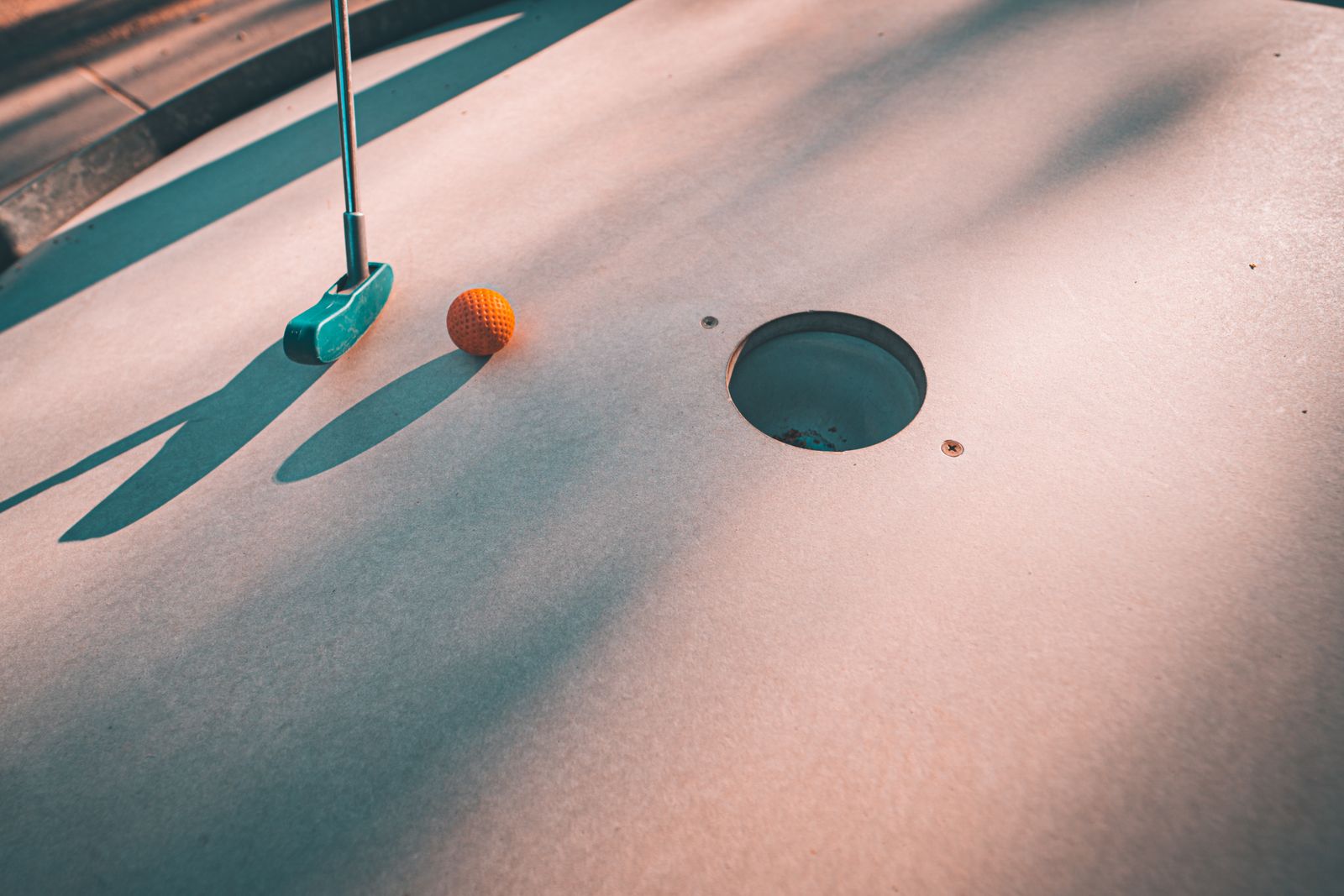 Minigolfklubba och orange boll vid ett hål på en minigolfbana