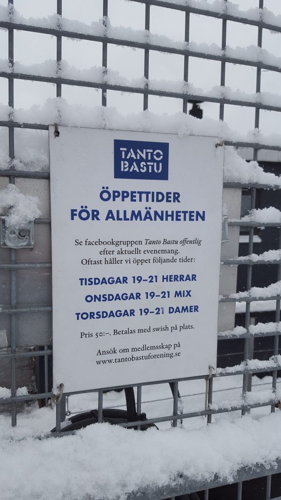 Skylt med rubriken Tanto Bastu och allmänhetens öppettider, uppsatt på ett snötäckt staket vid bastun