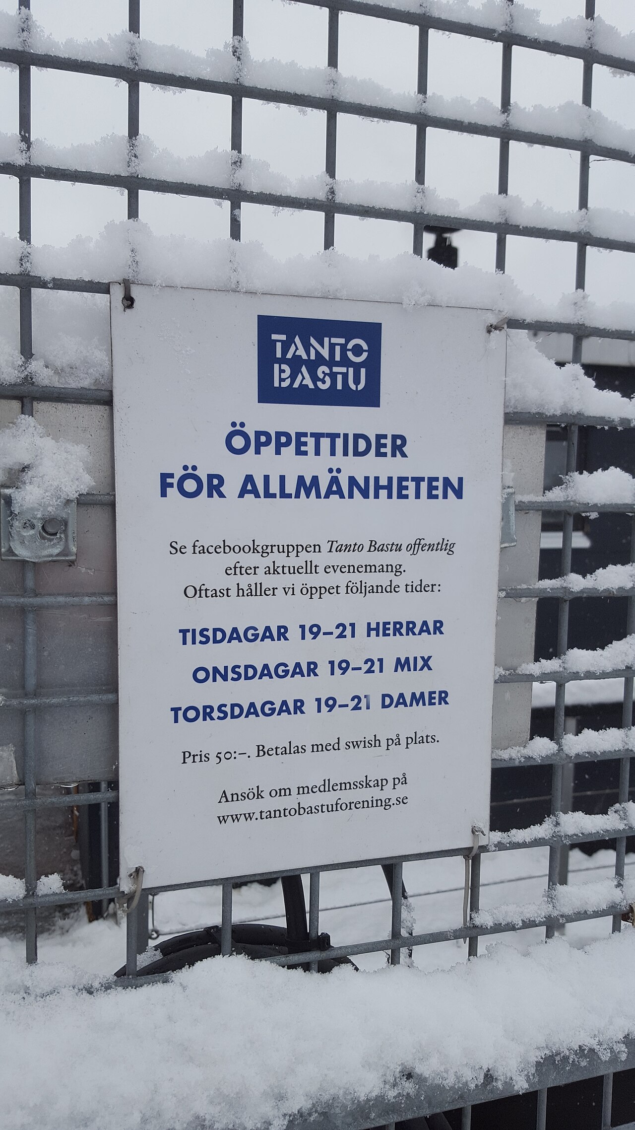 Skylt med rubriken Tanto Bastu och allmänhetens öppettider, uppsatt på ett snötäckt staket vid bastun
