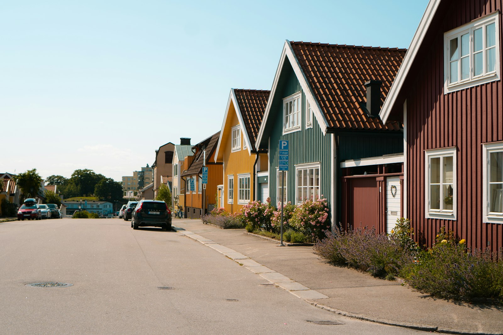Svensk småstadsgata med trähus i rött, grönt och gult och bilar parkerade längs trottoaren