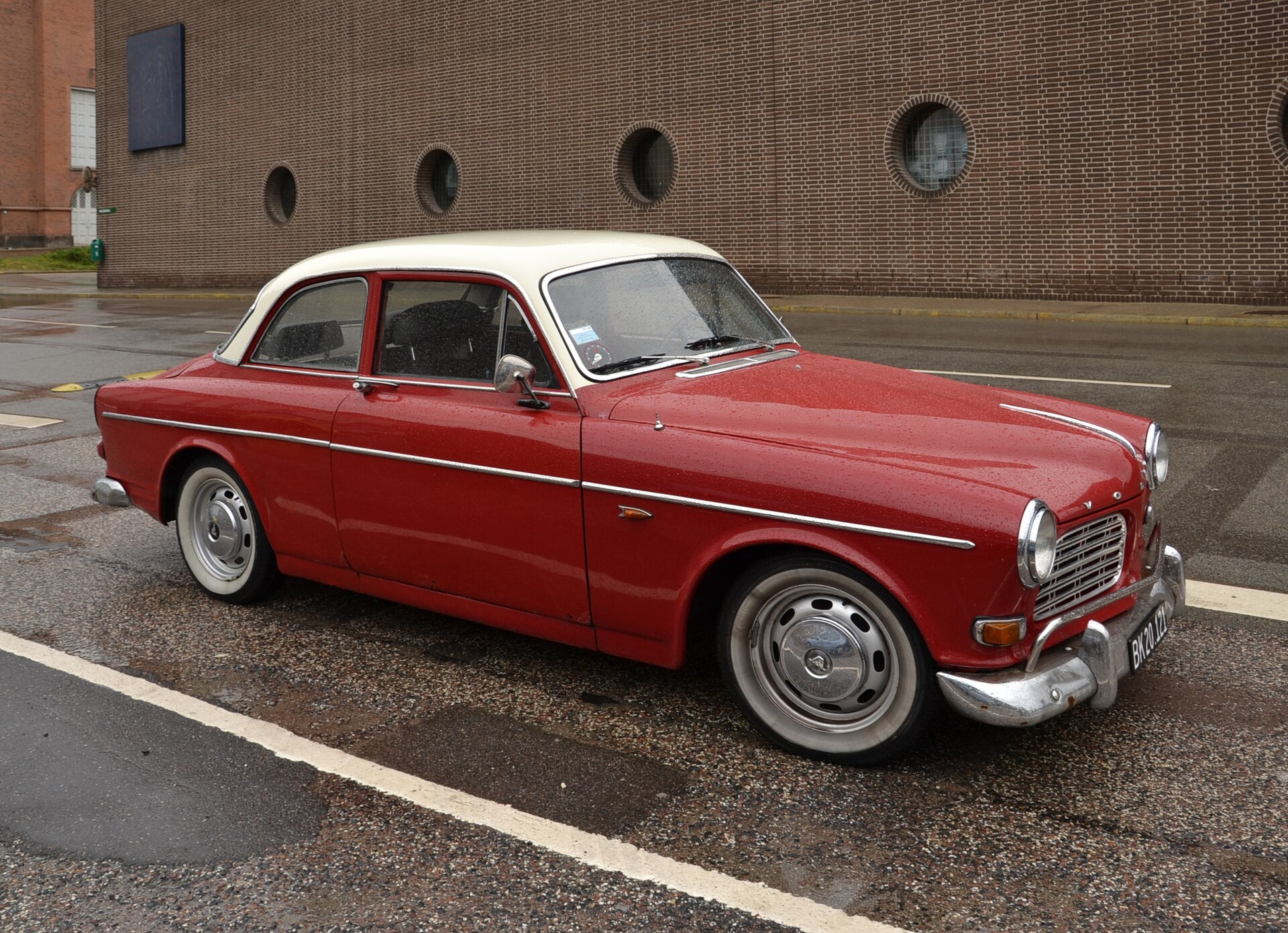 Röd Volvo Amazon med vitt tak parkerad på våt asfalt