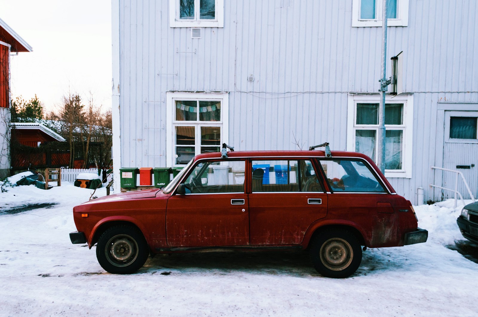 Röd kombibil parkerad i snön framför ett trähus