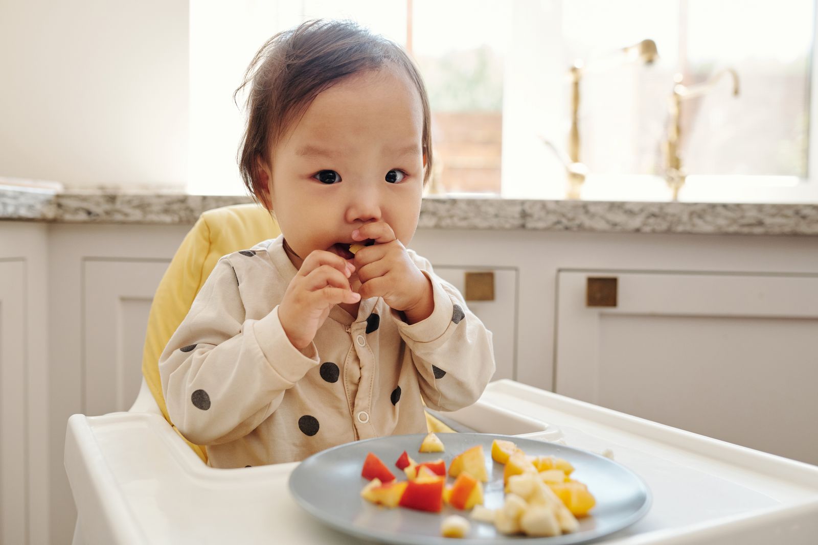 A toddler eating fruit and vegetables in a highchair