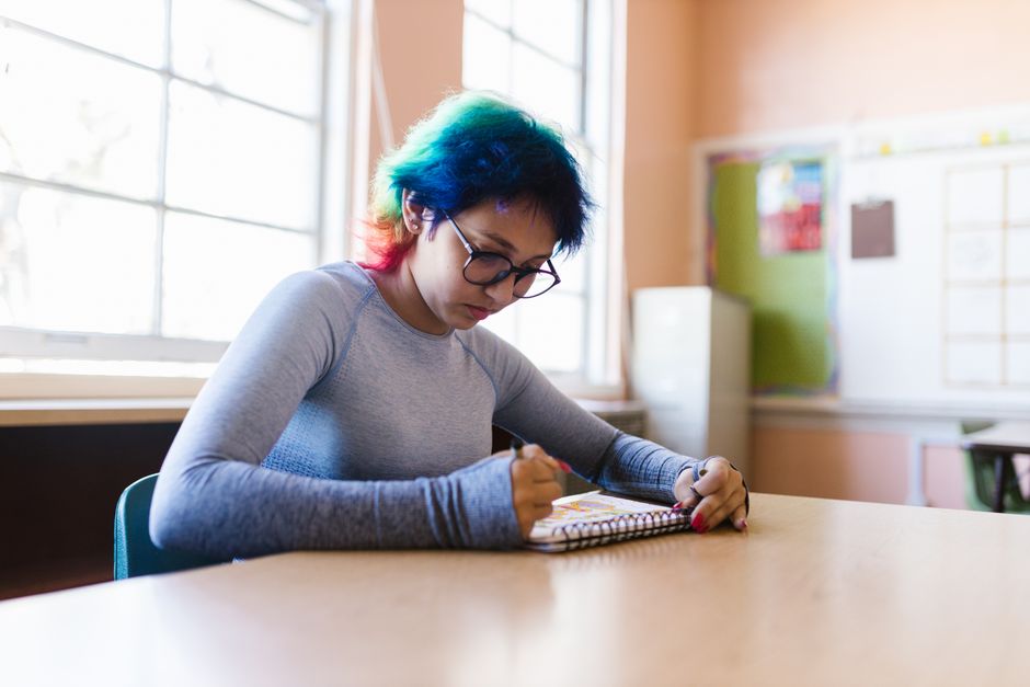 Elev som sitter vid ett bord i ett klassrum och skriver i ett block