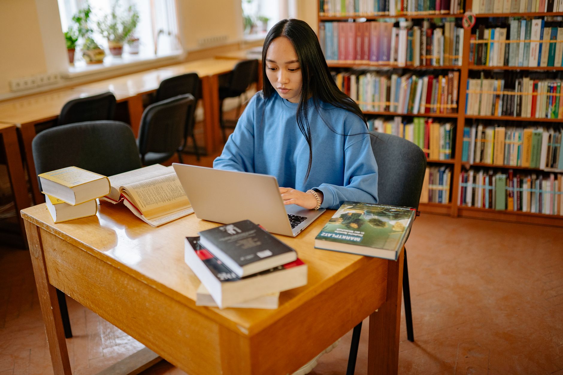 Elev i tonåren sitter med laptop och böcker vid ett bord i ett skolbibliotek