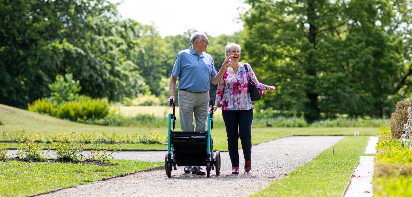 Äldre par på promenad utomhus med rollator i en grön park