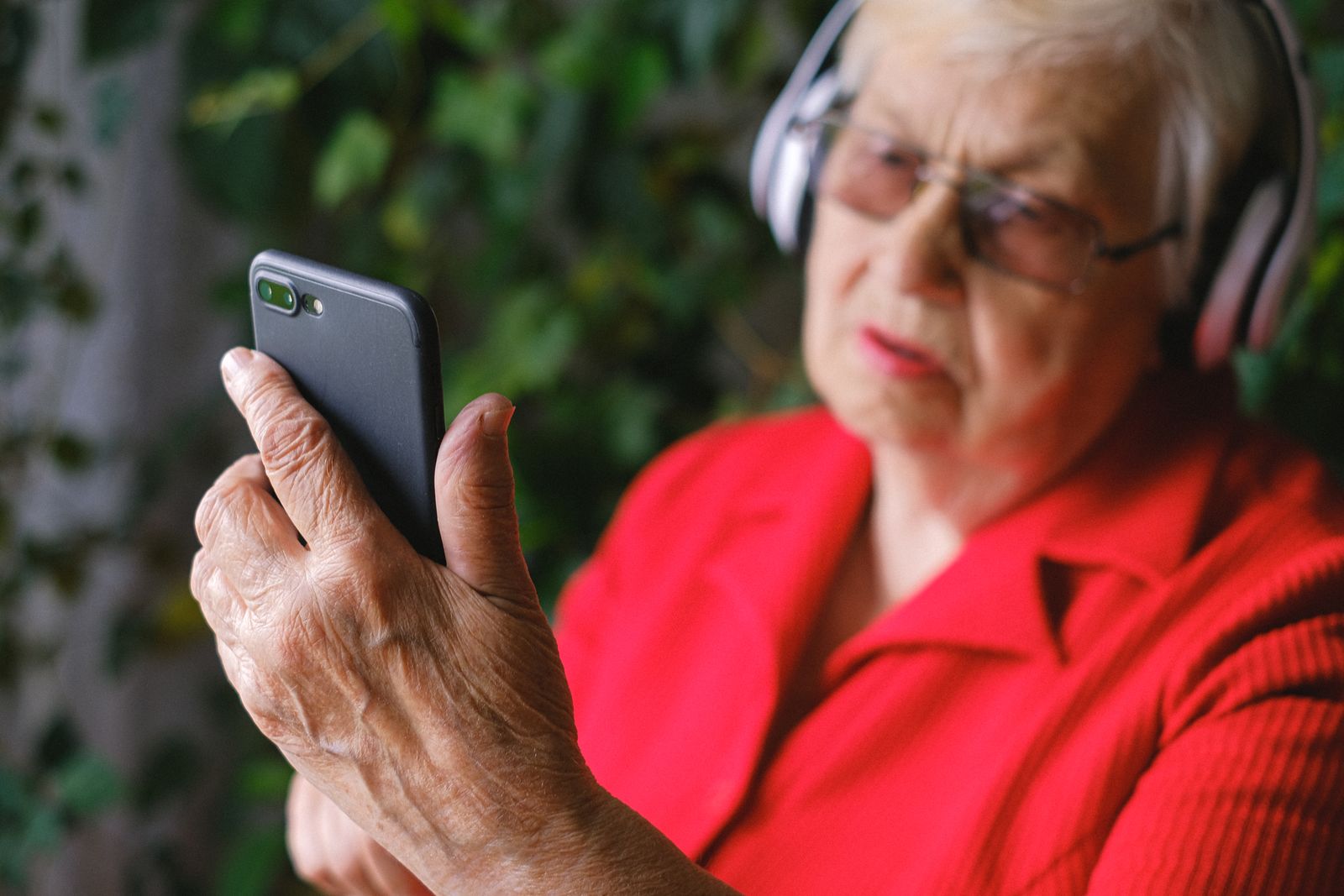 Äldre kvinna som lyssnar med hörlurar och håller i en telefon