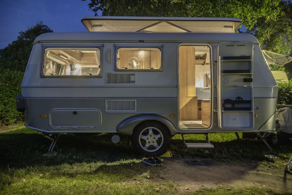 Liten husvagn med uppfällt tak lyser inifrån i skymningen på campingplats