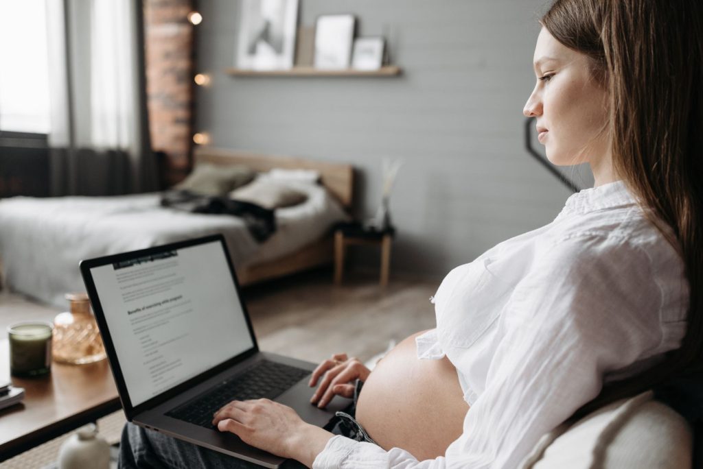 Gravid kvinna arbetar vid en bärbar dator i ett ljust hemmakontor