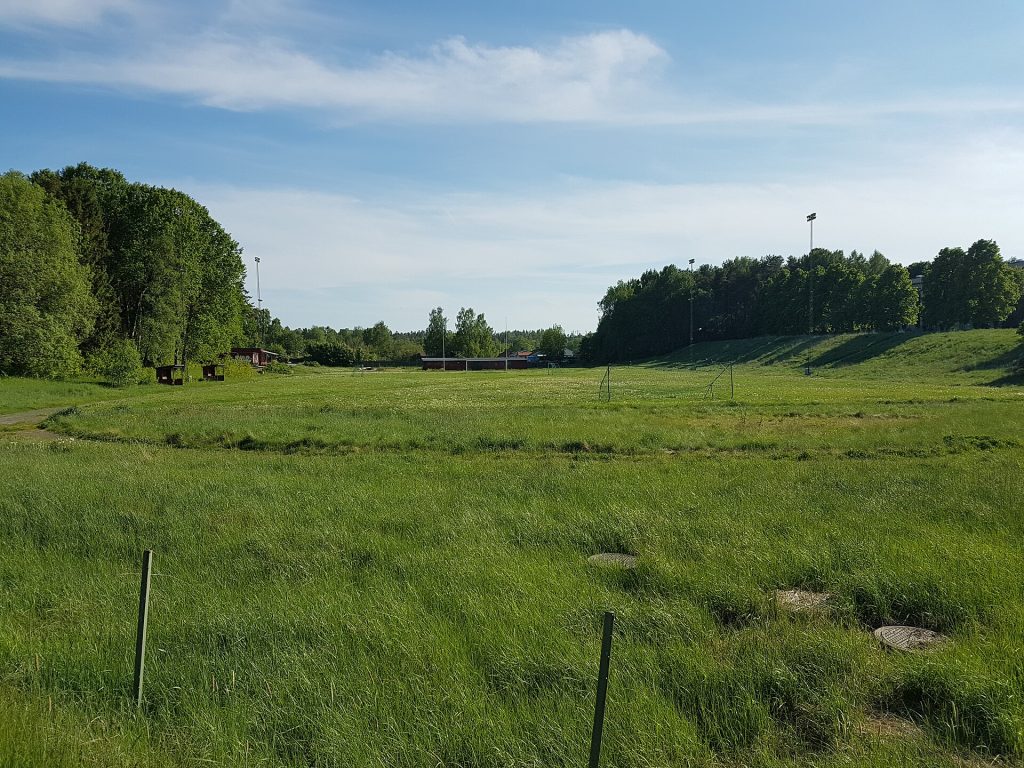Gräsplanen med fotbollsmål och belysningsmaster vid Ösmo idrottsplats en sommardag
