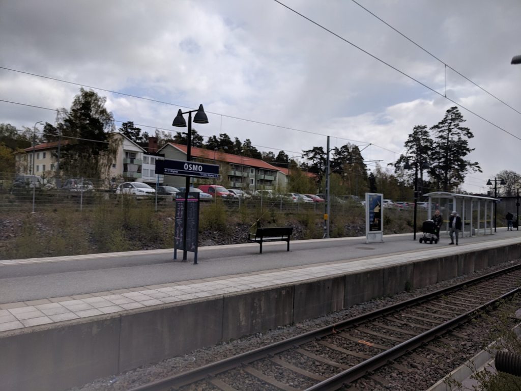Perrongen på Ösmo station med stationsskylten, en bänk och spåren i förgrunden.