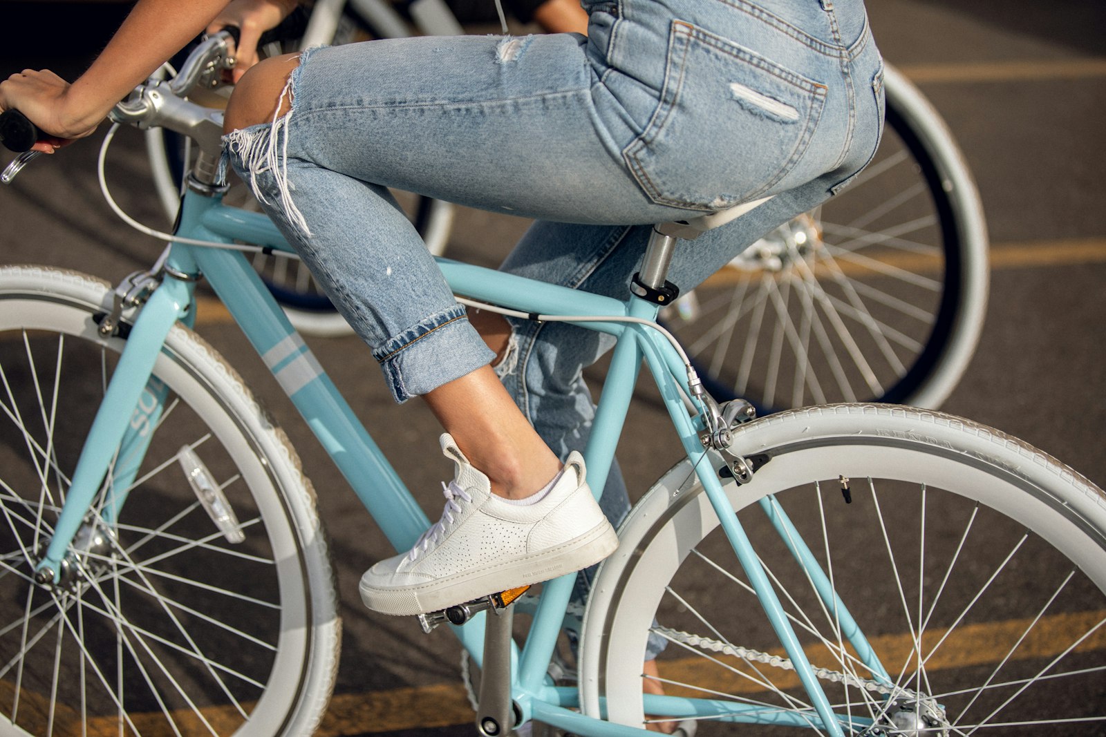 Stadscykel i turkos ram med en cyklist i jeans på en gata