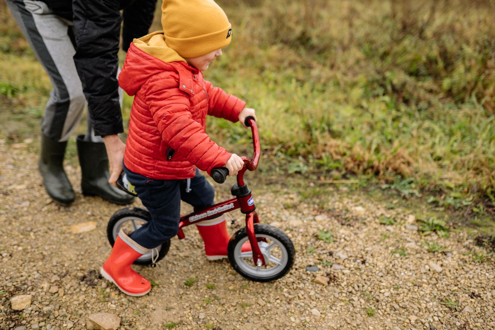 Litet barn i rod jacka pa en liten cykel pa en stig