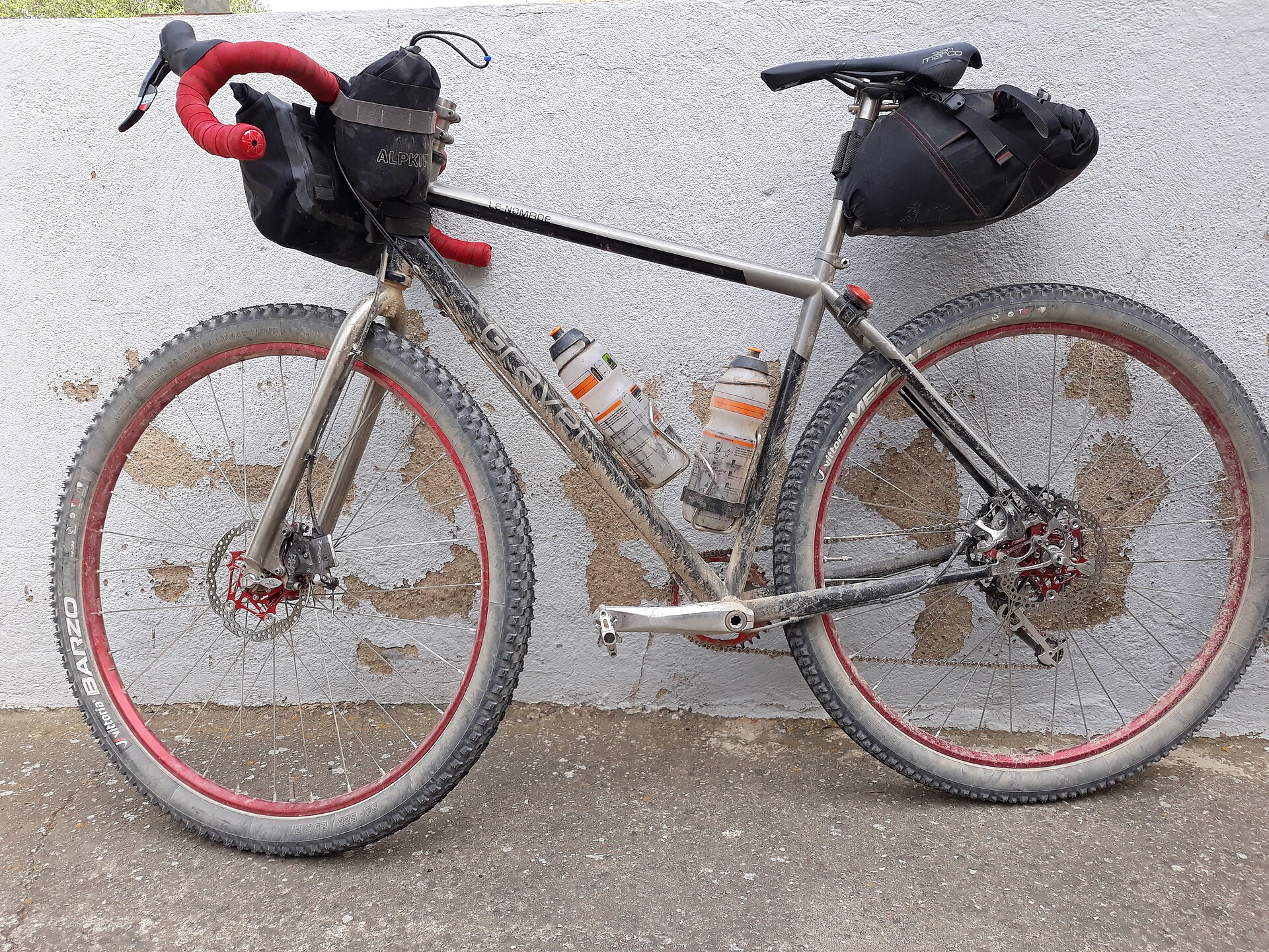 Gravelcykel med racerstyre, grova däck och packväskor på styret, ramen och under sadeln i stället för på en pakethållare