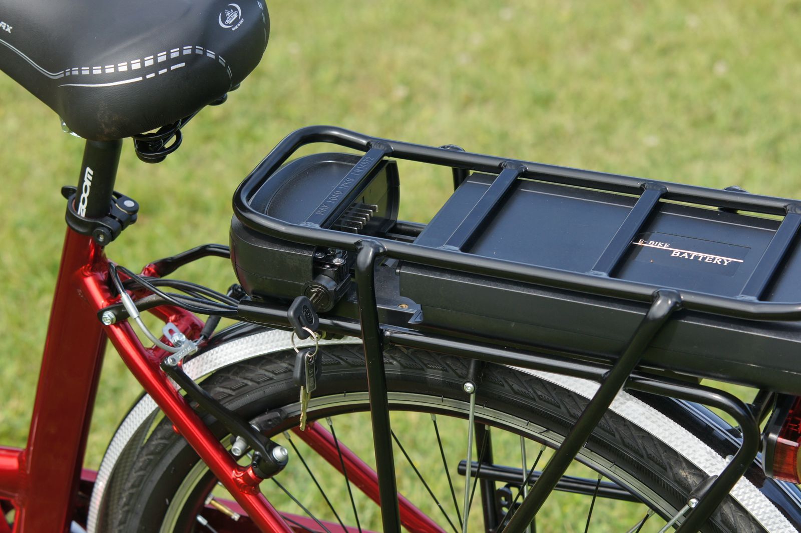 Avtagbart elcykelbatteri monterat på pakethållaren på en röd elcykel, med nyckeln i låset