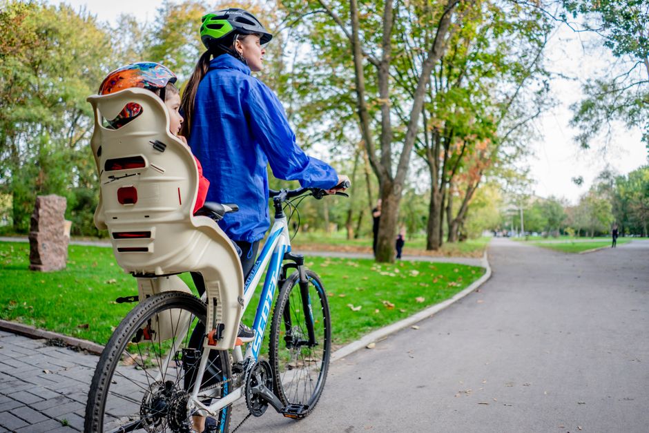 Kvinna med cykelhjälm på cykel med barn i bakmonterad cykelbarnstol i en park