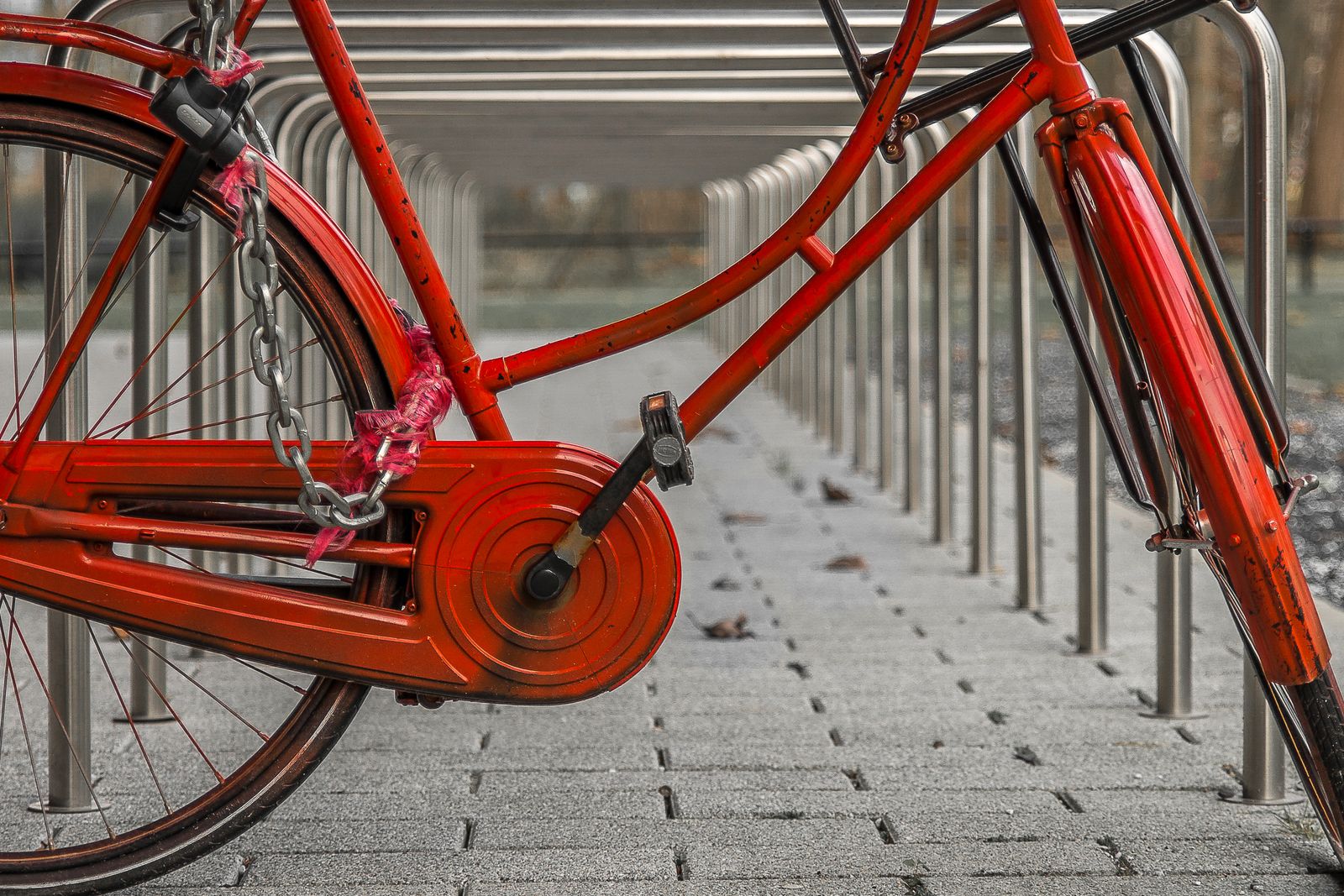 Röd cykel fastlåst med ett kättinglås vid ett cykelställ